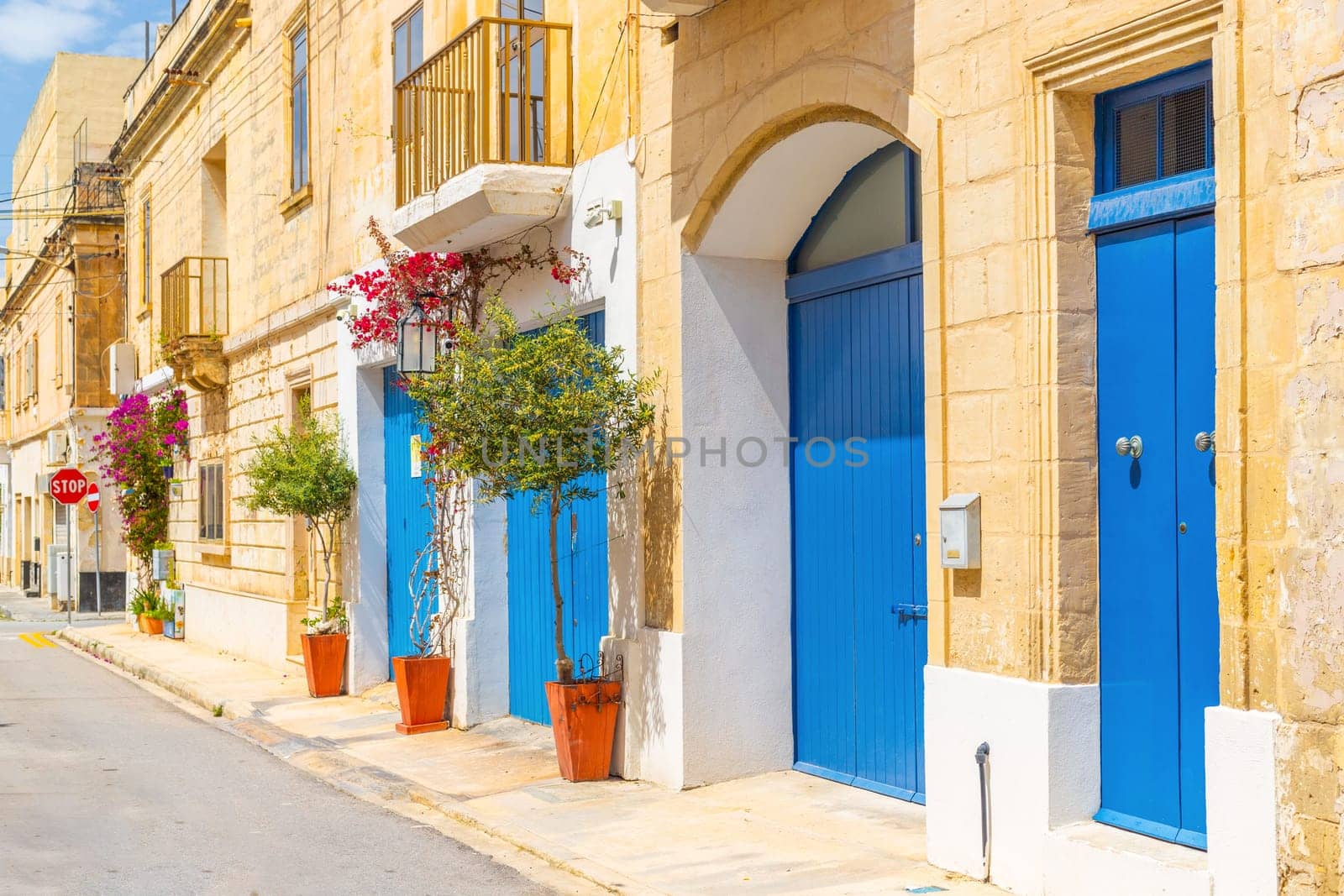 View of an empty typical Maltese street with potted trees near blue wooden garage doors