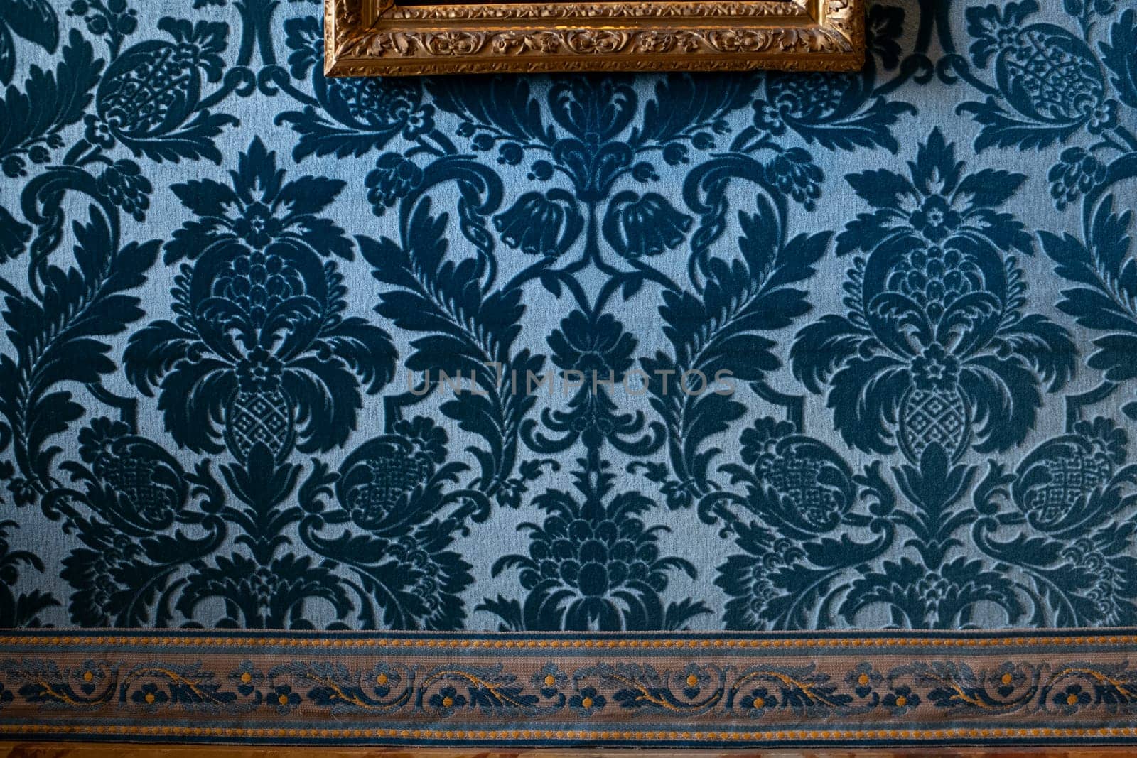 Blue velvet wallpaper and gold frames with paintings in castle