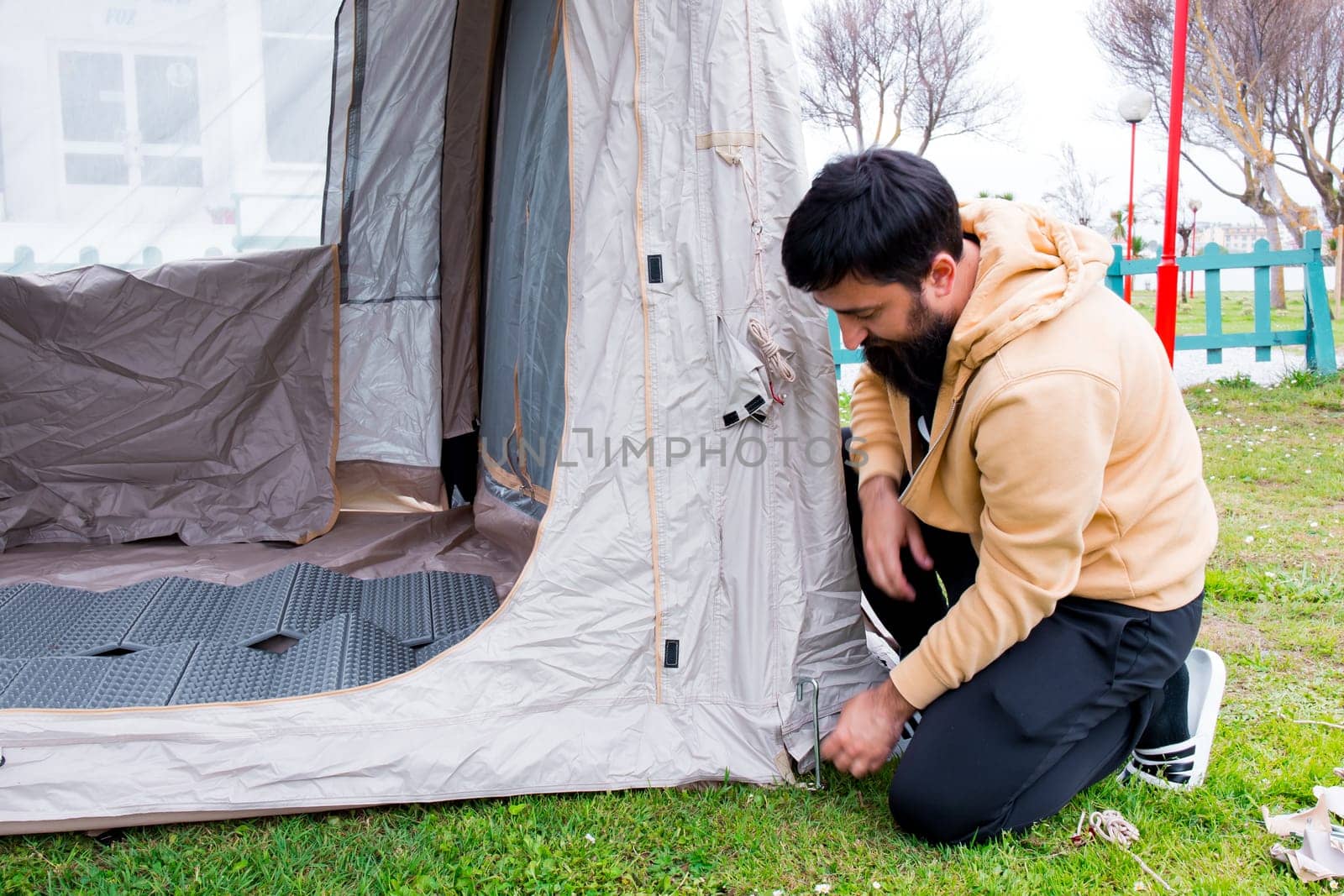 Young hispanic male camping solo assembling tent outdoors.