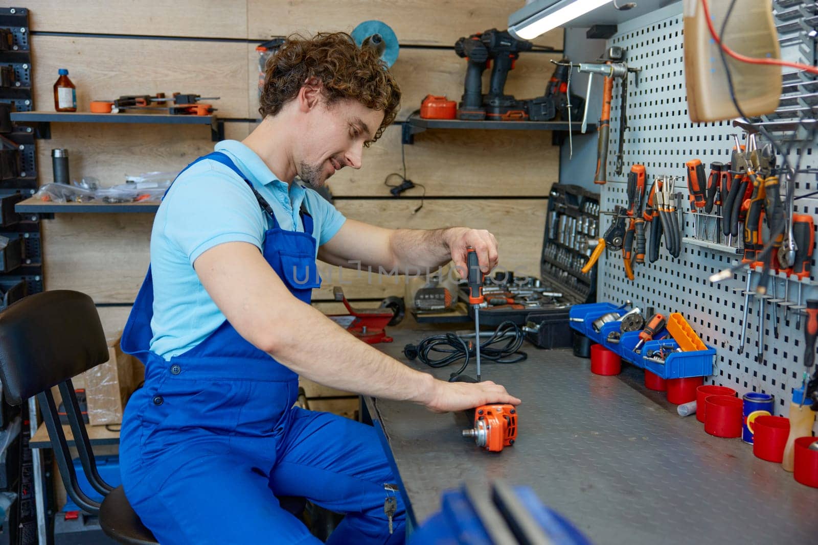 Professional repairman fixing electrical angle grinder working with screwdriver at workshop. Repair shop for broken power tools