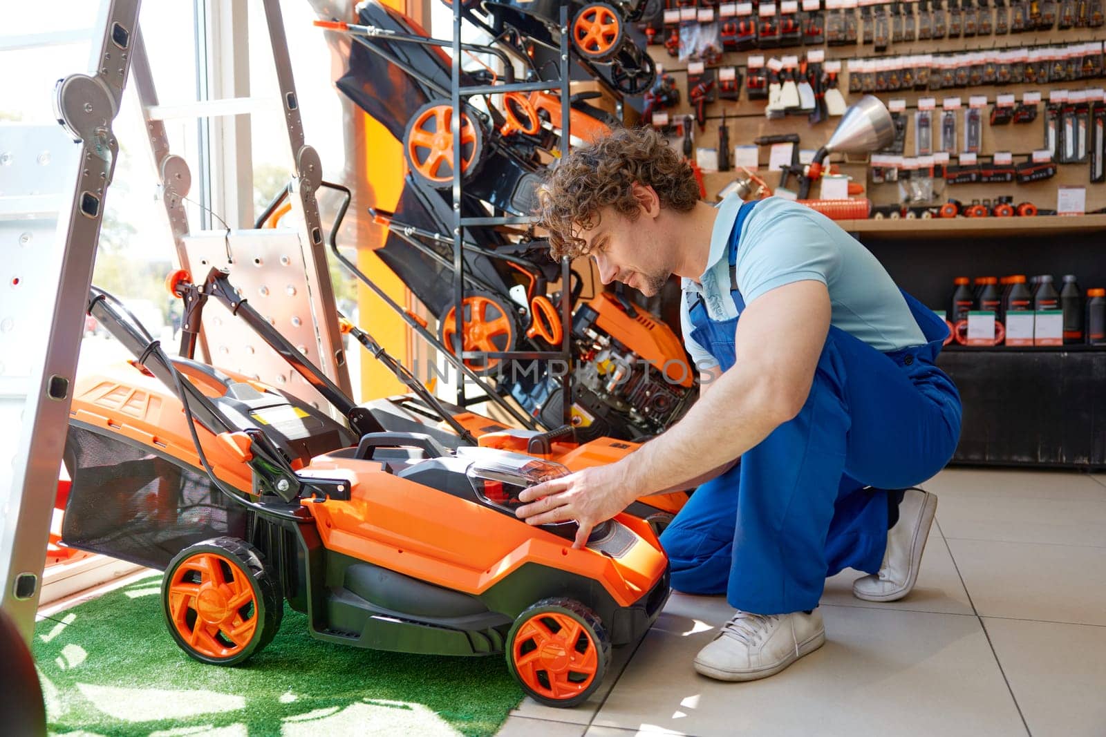 Young workman choosing and testing electric lawnmower at garden supply store. Consumer buying modern motor grass cutter at hardware supermarket
