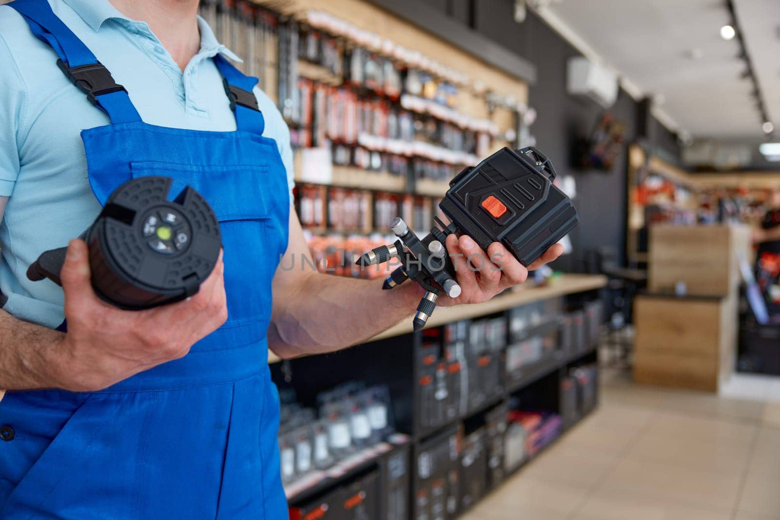 Young salesman wearing uniform checking laser level manual tool selective focus. Retail business and hardware store