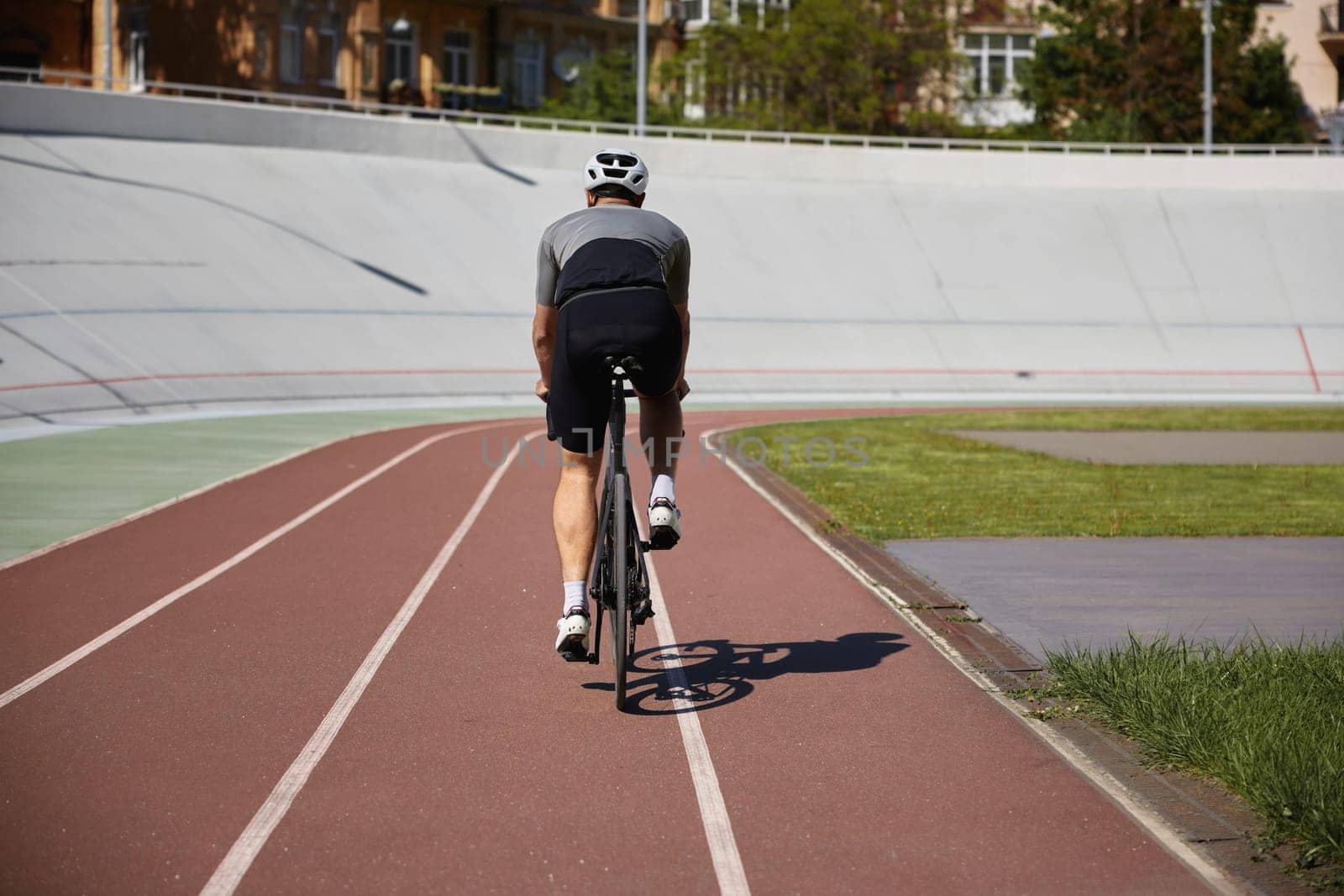Back view man bicyclist enjoying recreational pursuit riding triathlon bike on empty velodrome road. Active lifestyle and sports hobby concept