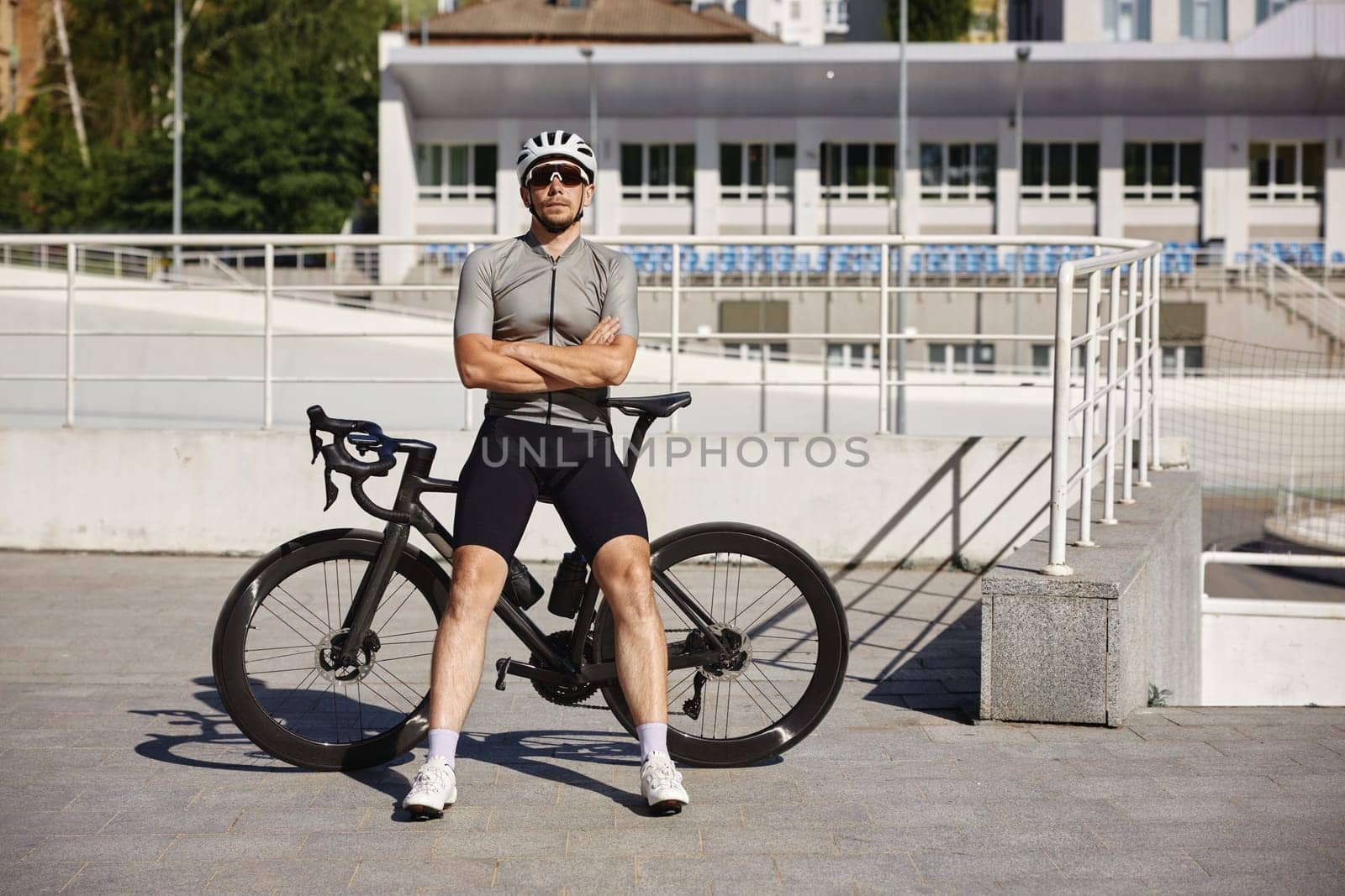 Well-equipped male cyclist wearing activewear, sunglasses and protective headgear came to urban velodrome for training during sunny summer day