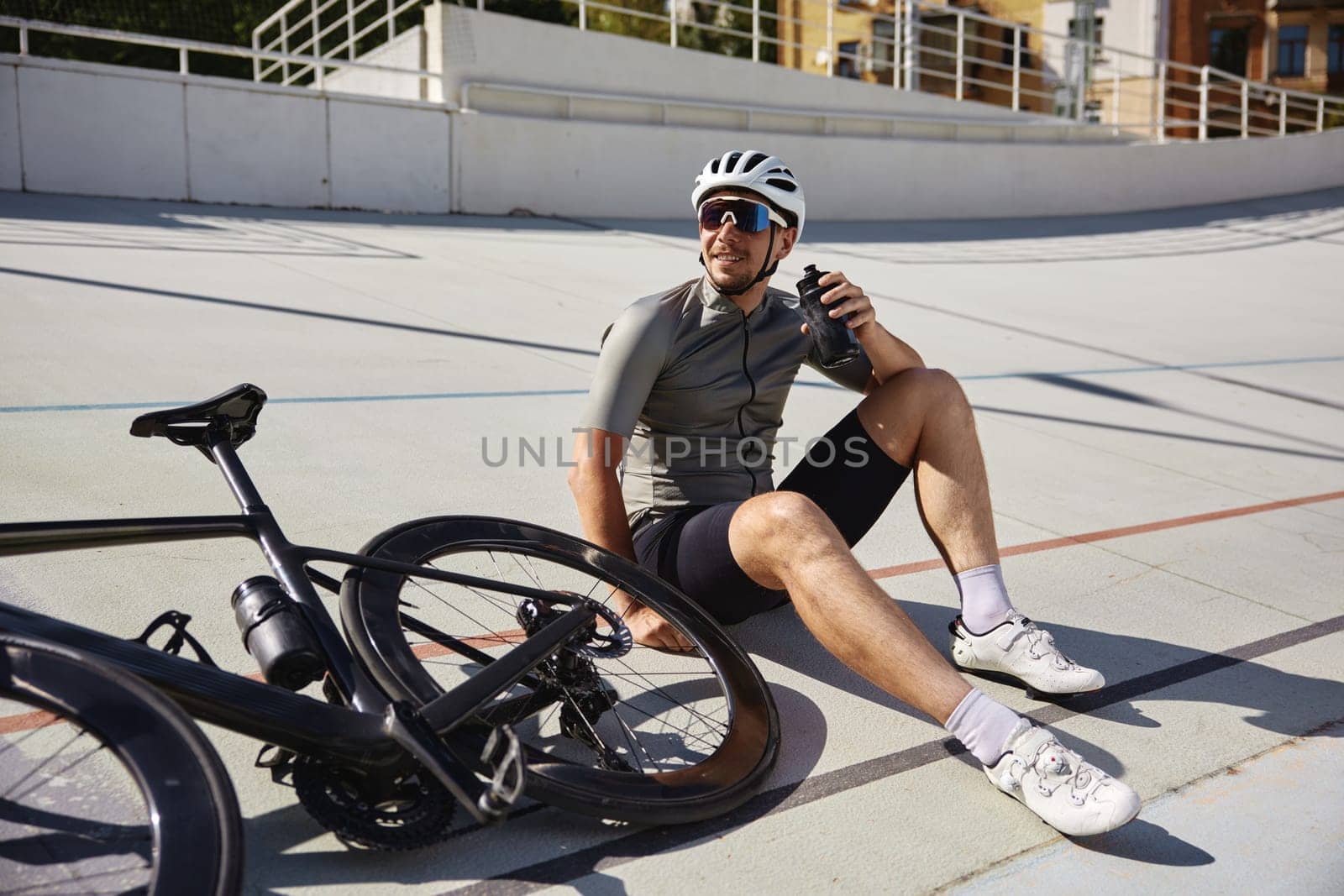 Happy tired sportsman with water bottle resting enjoying refreshing time during cycling training on open road sprint track