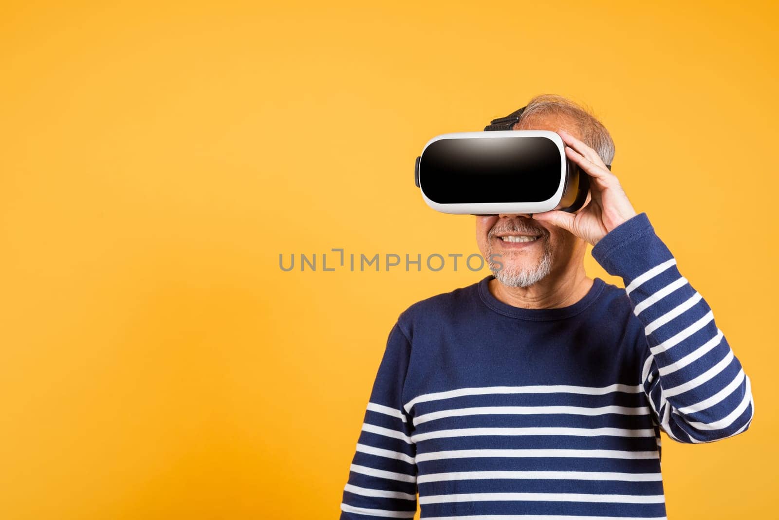 Portrait Asian smiling old man holding in a virtual reality glasses headset studio shot isolated yellow background, Excited happy senior man pensioner using VR play simulation game