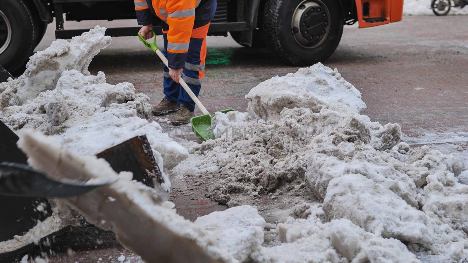 Road worker cleaning street from snow with a shovel next to a truck after heavy snowfall