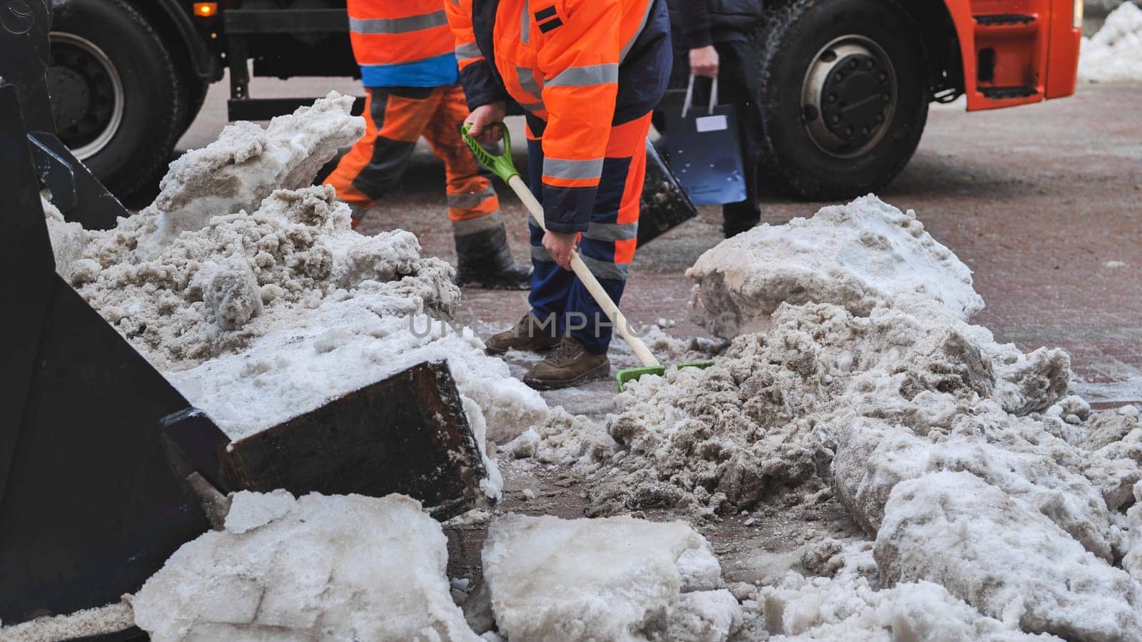 Road workers cleaning city street from snow with shovels and truck in winter