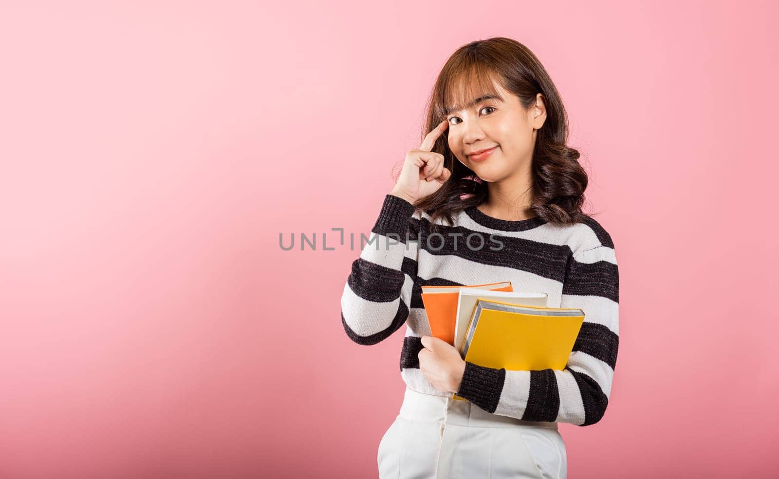 Portrait of beautiful Asian young woman teenage smiling hugging books, female person holding book and thinking idea, studio shot isolated on pink background with copy space, education concept