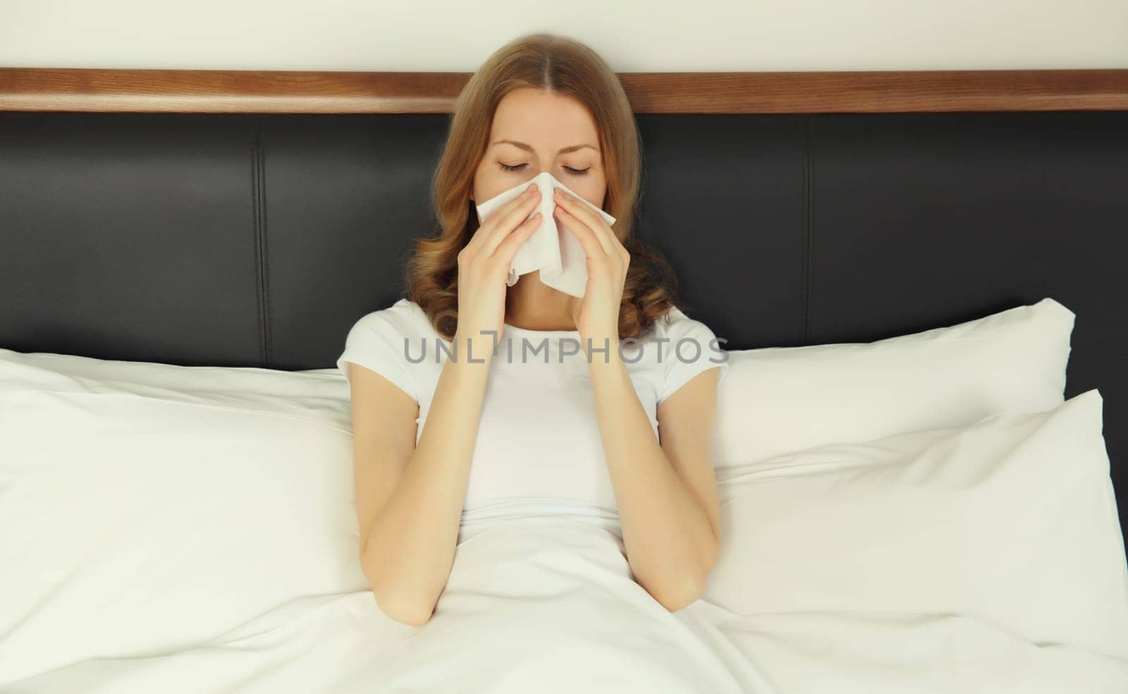 Sick exhausted young woman sneezing blow nose using tissue, unhealthy suffering girl feels unwell lying on bed at home