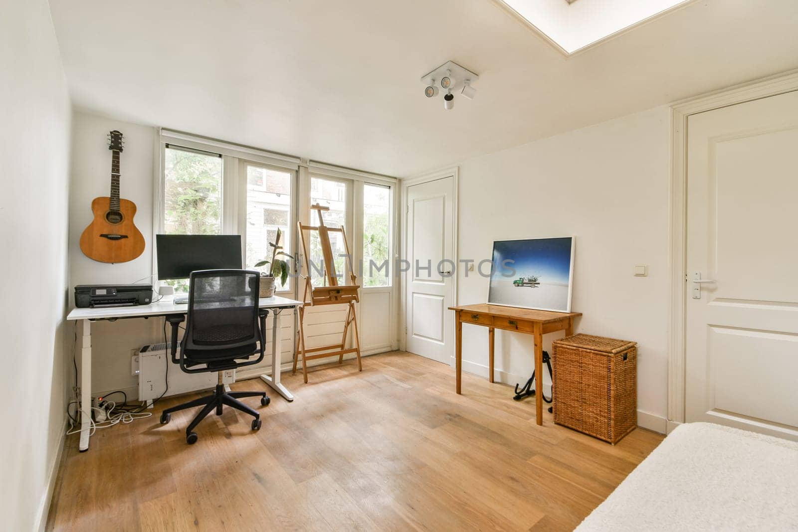 A clean and bright home office featuring a desk with a computer, acoustic guitar, and natural light from large windows. A perfect blend of functionality and style.