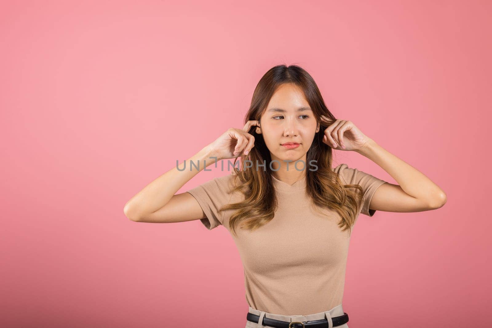 Woman bad mood pain her closed ears with finger and close eyes, Asian beautiful young female covers ears for loud noise, studio shot isolated on pink background with copy space, bad pressure
