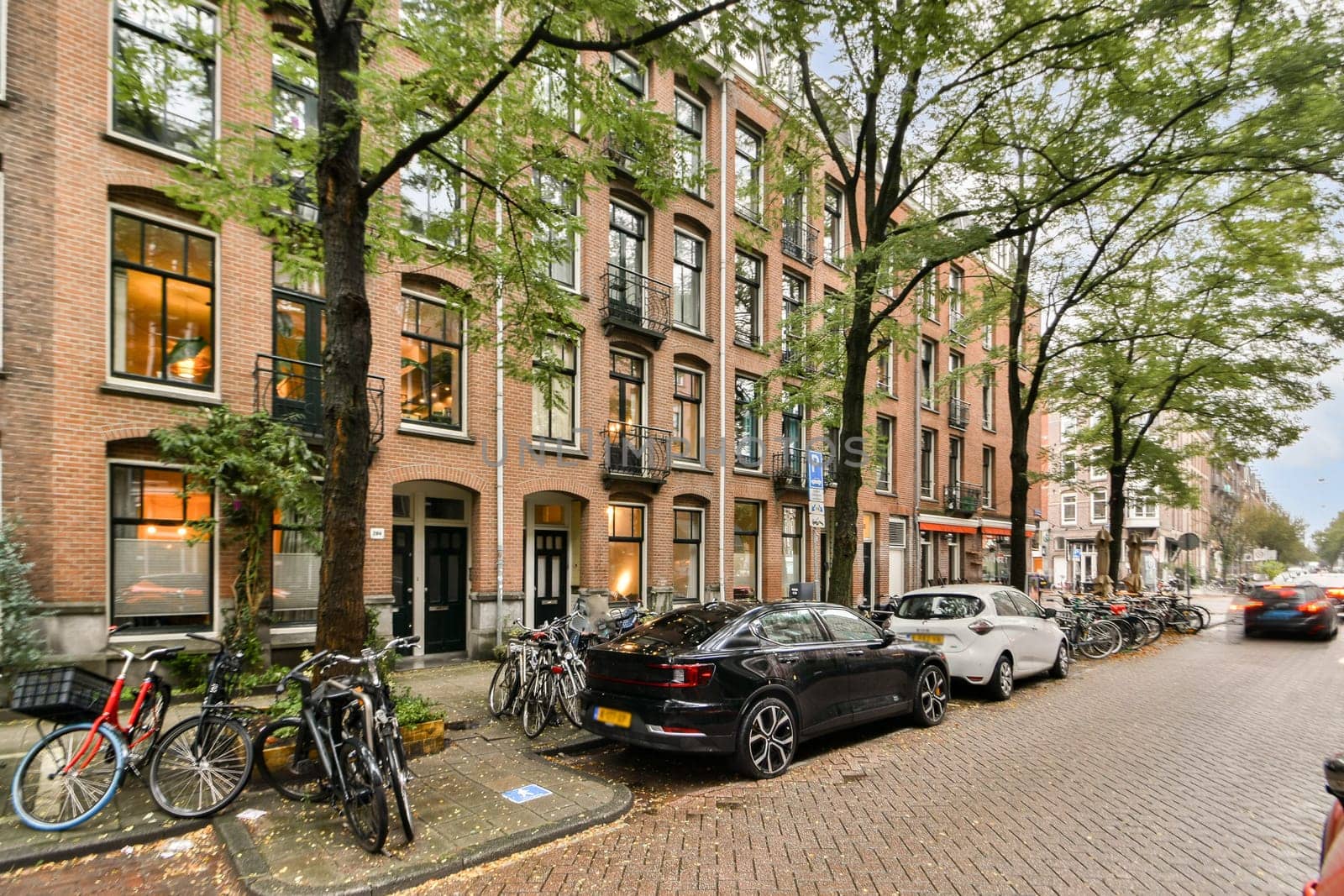 A picturesque view of a tree-lined street featuring classic brick buildings, parked bicycles, and cars, evoking a cozy urban atmosphere.