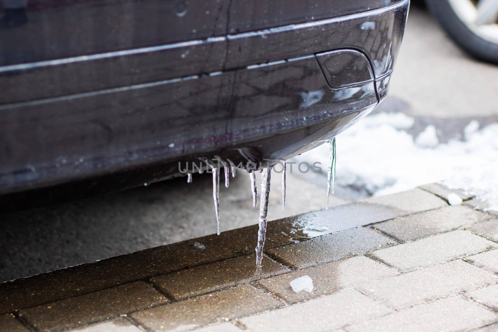 Long icicles are hanging from the exhaust pipe of a car due to the extremely cold weather conditions during winter season