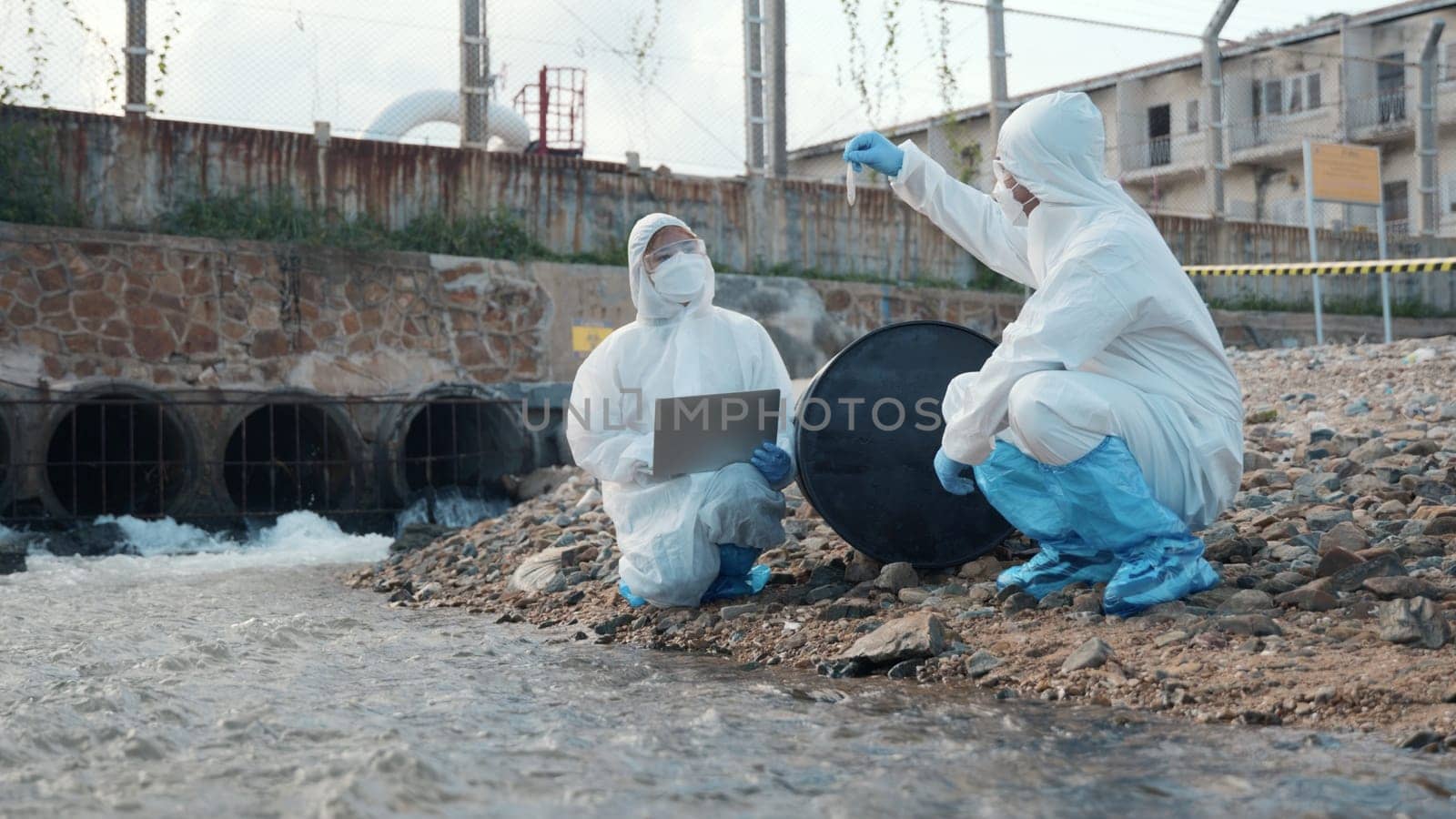 Ecologist sample water from the river and get fishes dead to check effected case in laboratory, Biologist wear protect suit and mask collects sample of waste water from industrial, problem environment
