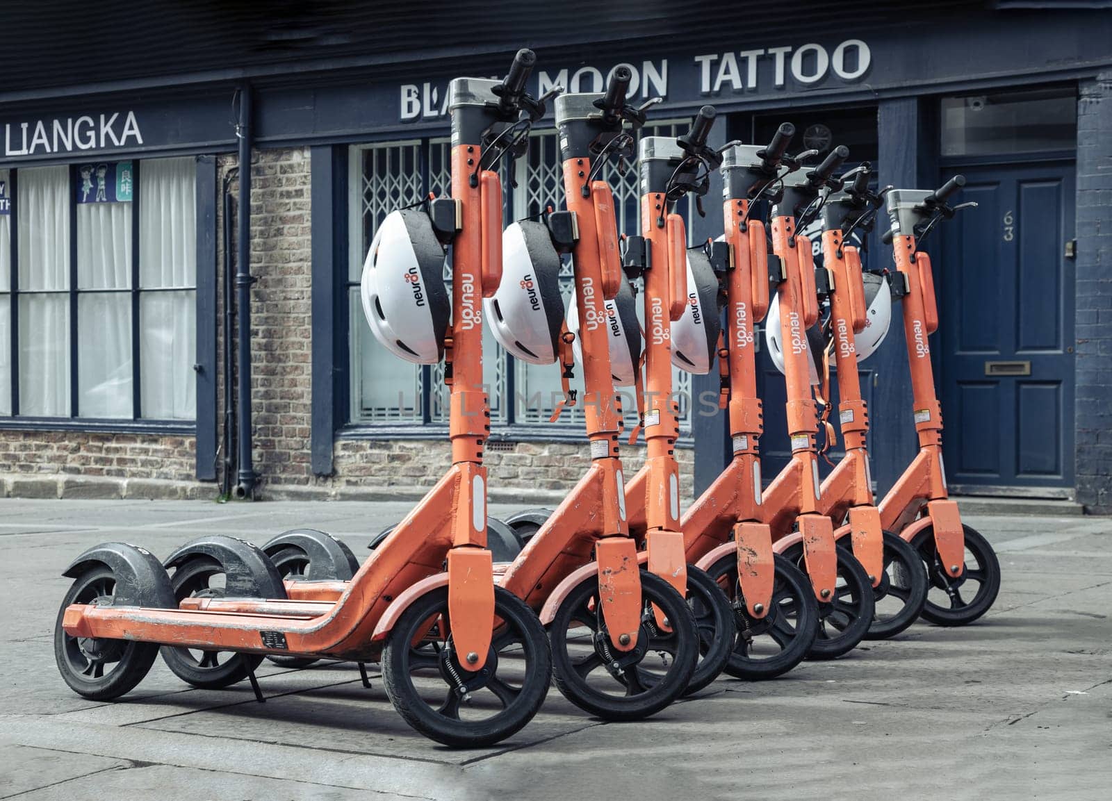 Newcastle, UK - Apr 14, 2025 - Bright orange electric scooters with white safety helmets parked on the sidewalk in downtown. Public rental e-scooter for trip and travel in center city, use it as your Wallpaper, Poster and Space for text, Selective focus.