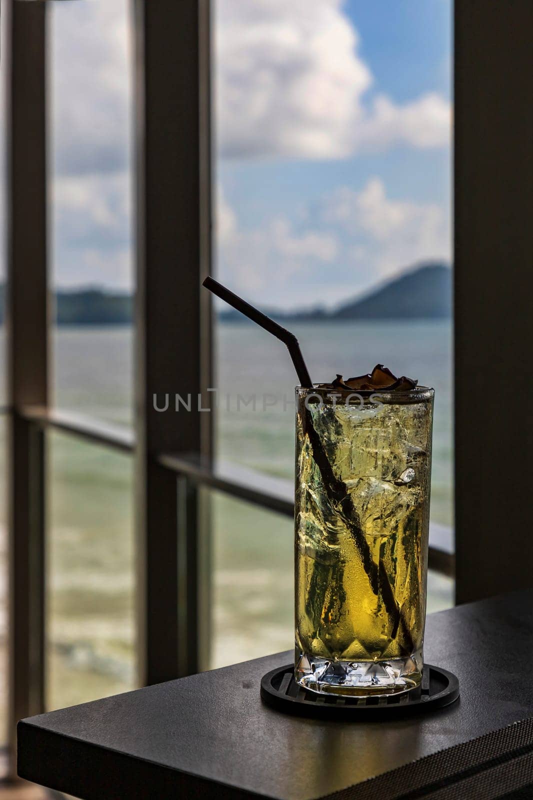 A glass of sweet and refreshing water is placed on a table on a wooden balcony in a restaurant by the sea. the background is the sea The mountain and blue sky are cloudy during the day.Selective focus