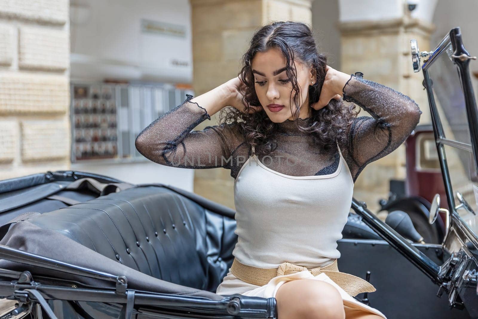Beautiful long black hair girl is posing on the vintage car looking down. Horizontally.