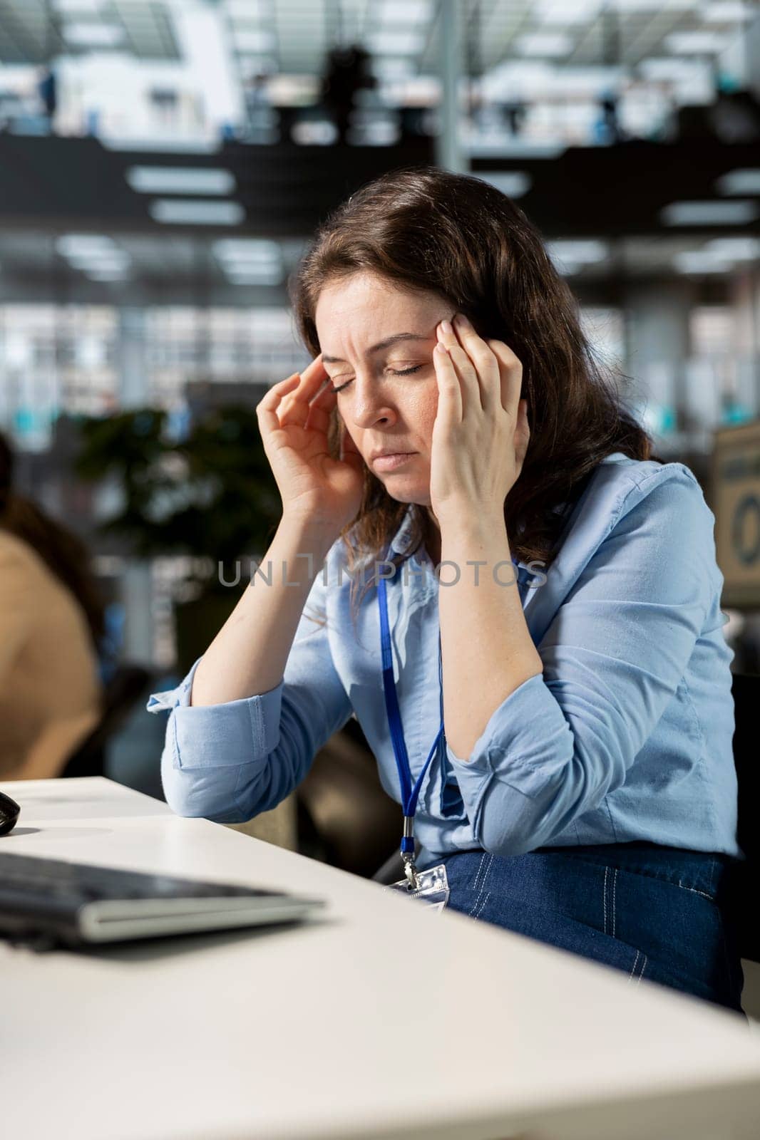 Exhausted overworked woman being unwell with a migraine at the office, trying to overcome stress and pressure but feeling unhappy. Worried tired employee with a serious headache.