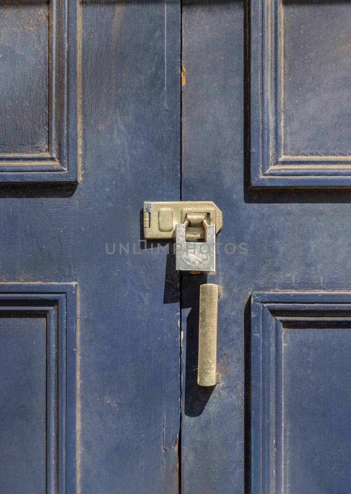 Newcastle, UK - Apr 13, 2025 - Silver colour locked padlock in Brass door lock hasp latch on the blue painted wooden door frame. Storage security, use it as your Wallpaper, Poster and Space for text, Selective focus.