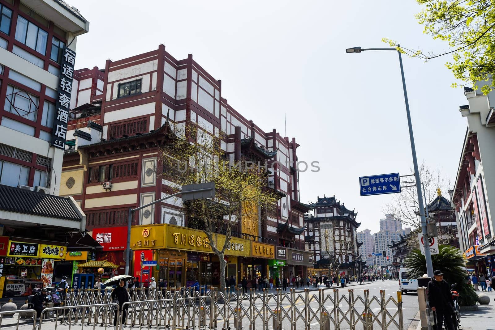 Shanghai, China - 1 April 2025: City street in Shanghai with traditional Chinese architecture, shops and pedestrians. Sunny day with carved decorations and red accents on buildings.