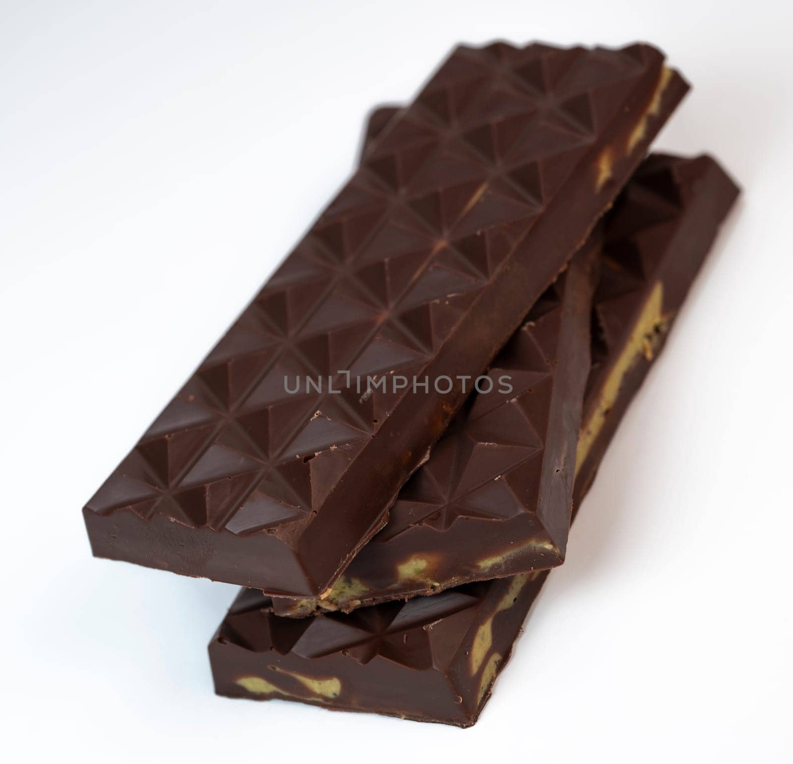Stacked layers of kadaif embrace a generous coating of rich chocolate and are topped with a pistachio, showcasing the delightful texture and flavors in a culinary presentation.
