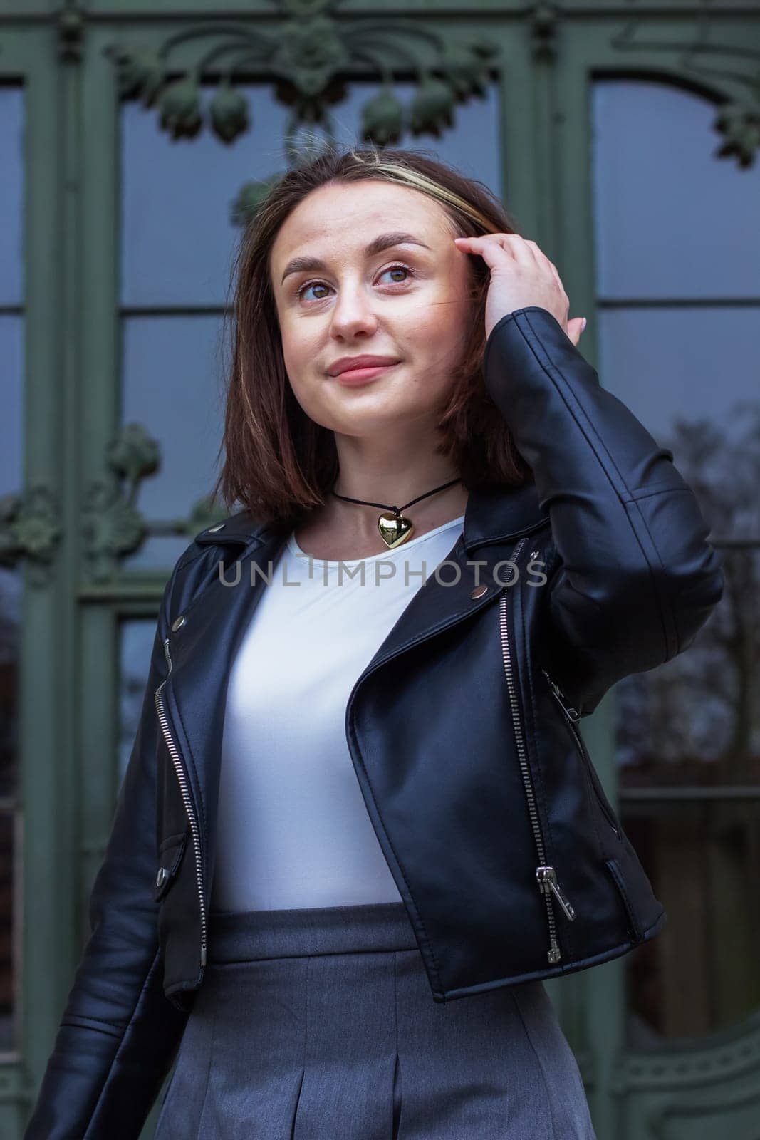 Portrait of a young beautiful woman straightening her hair with her hand and smiling against the background of a wooden green carved door. High quality photo