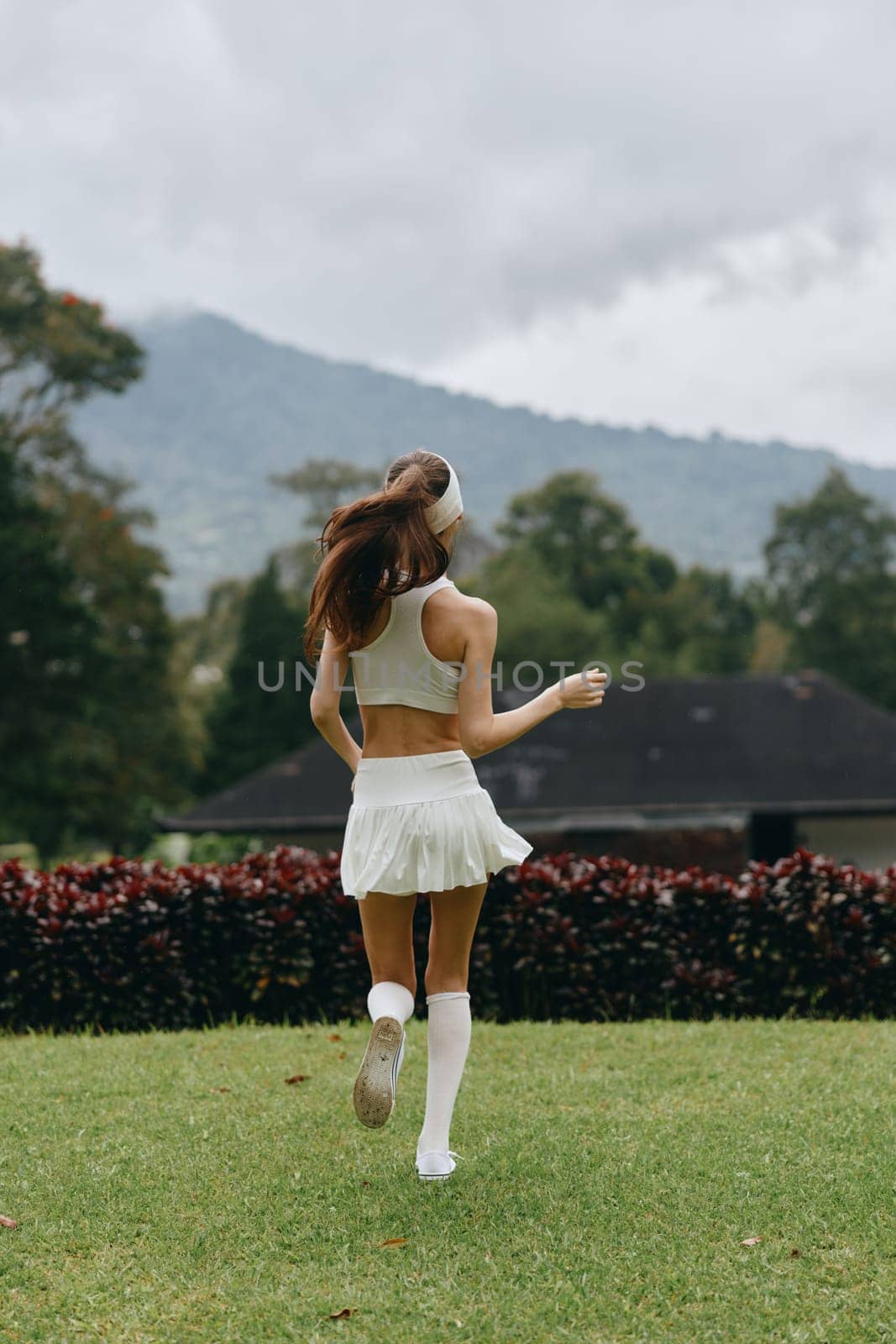 Energetic young model dressed in white activewear runs through a picturesque green park, reflecting joy, health, and an active lifestyle amidst a serene backdrop of nature