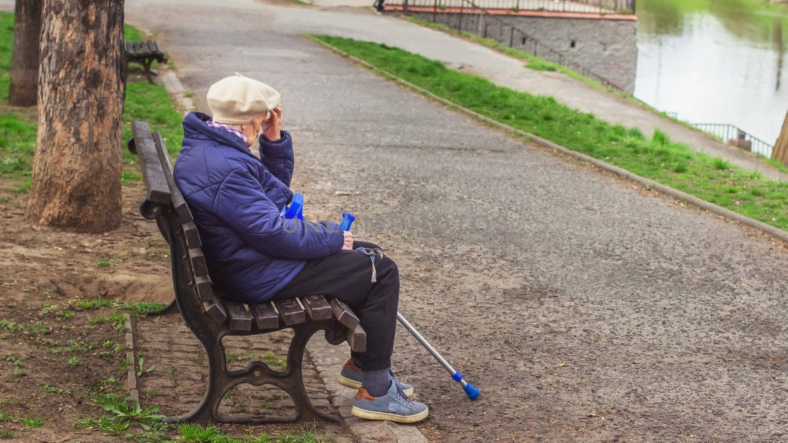 Poland, Wroclaw, April 13, 2025. A lonely old woman pensioner with a cane sits on a bench in the park. High quality photo