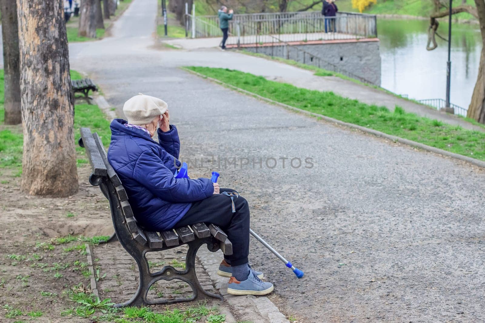 Poland, Wroclaw, April 13, 2025. A lonely old woman pensioner with a cane sits on a bench in the park. High quality photo