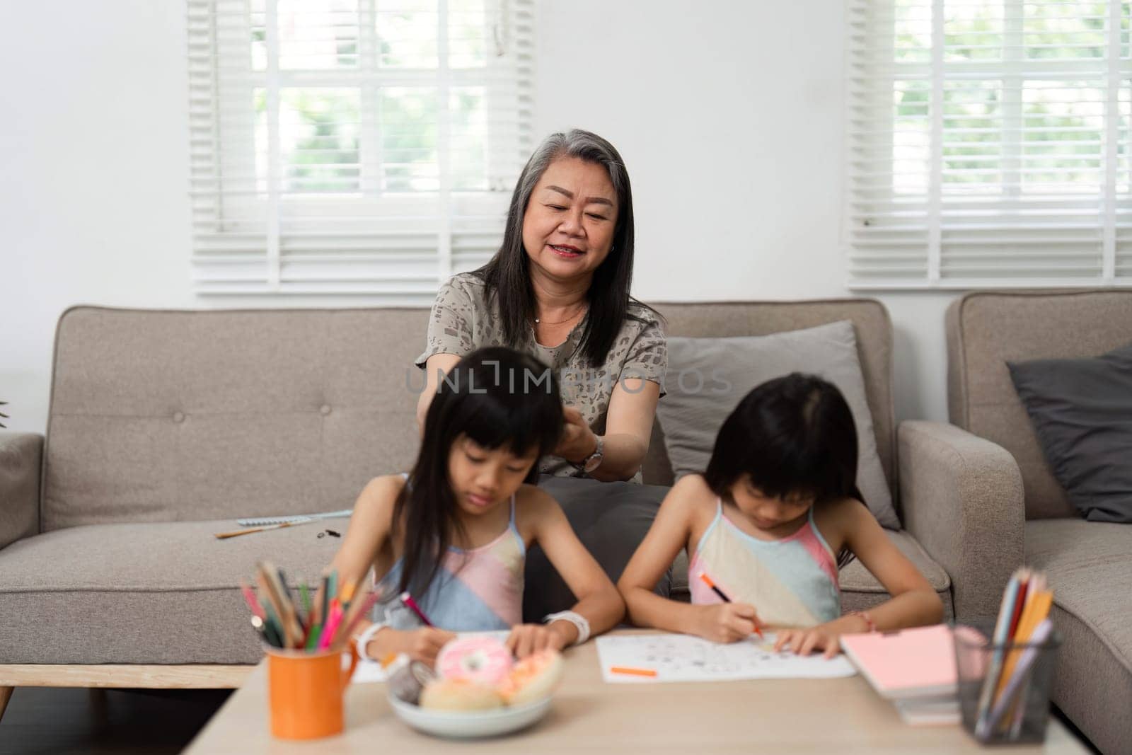 A grandmother lovingly engages with her granddaughters as they create art, fostering a supportive and creative environment at home.
