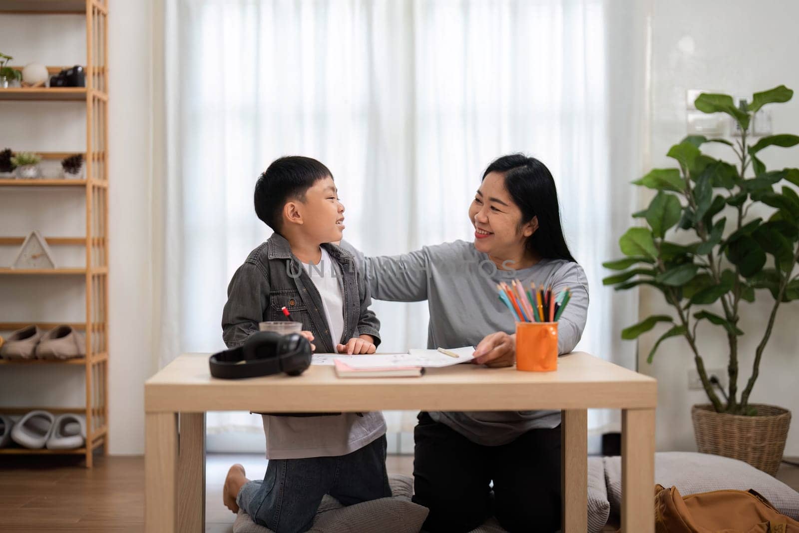 A mother and her son share a joyful moment as they work on school assignments together, fostering a love for learning in a cozy home environment.