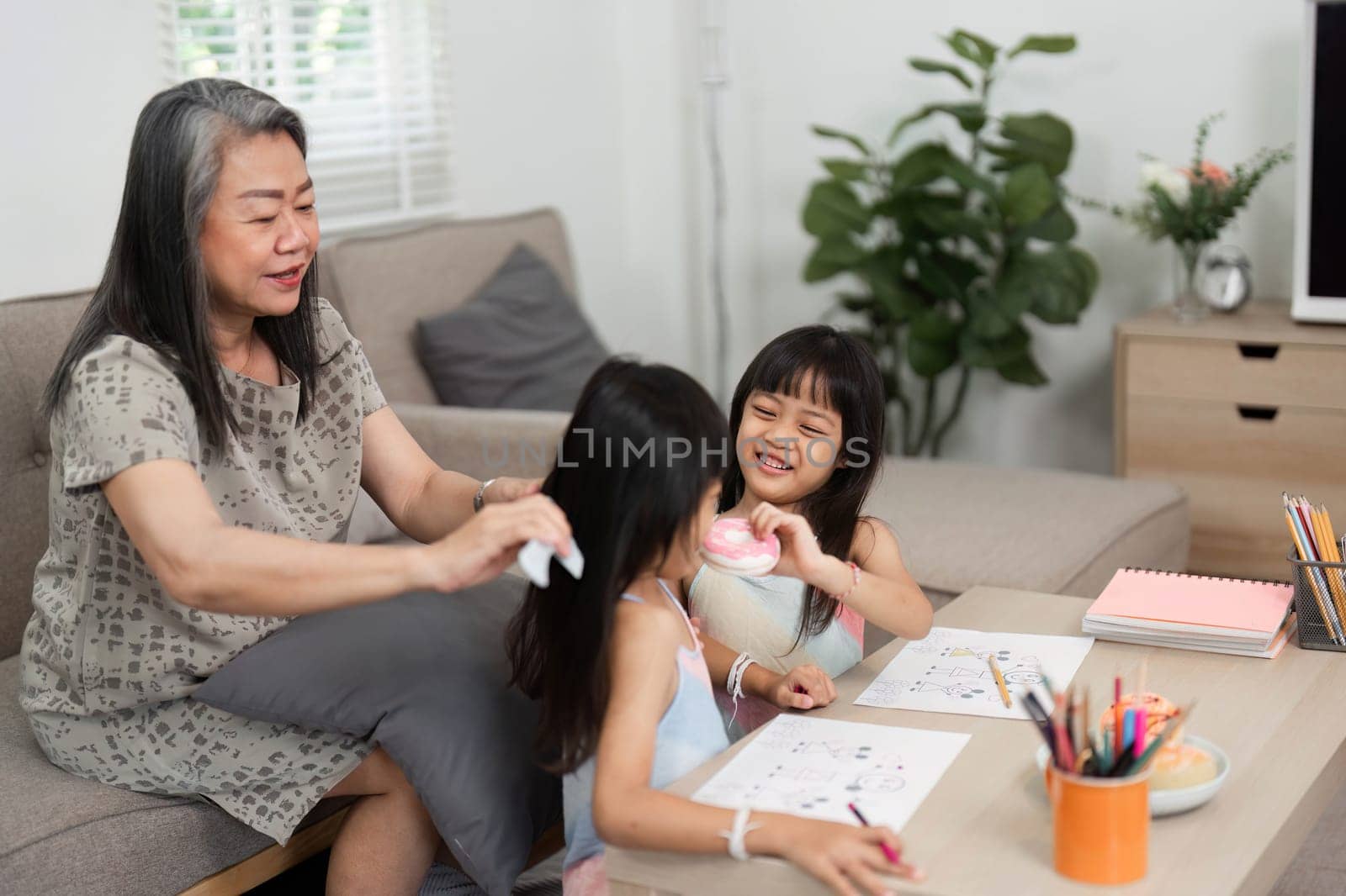 In a cozy living room, a grandmother lovingly assists her granddaughters as they explore their creativity through art and learning.