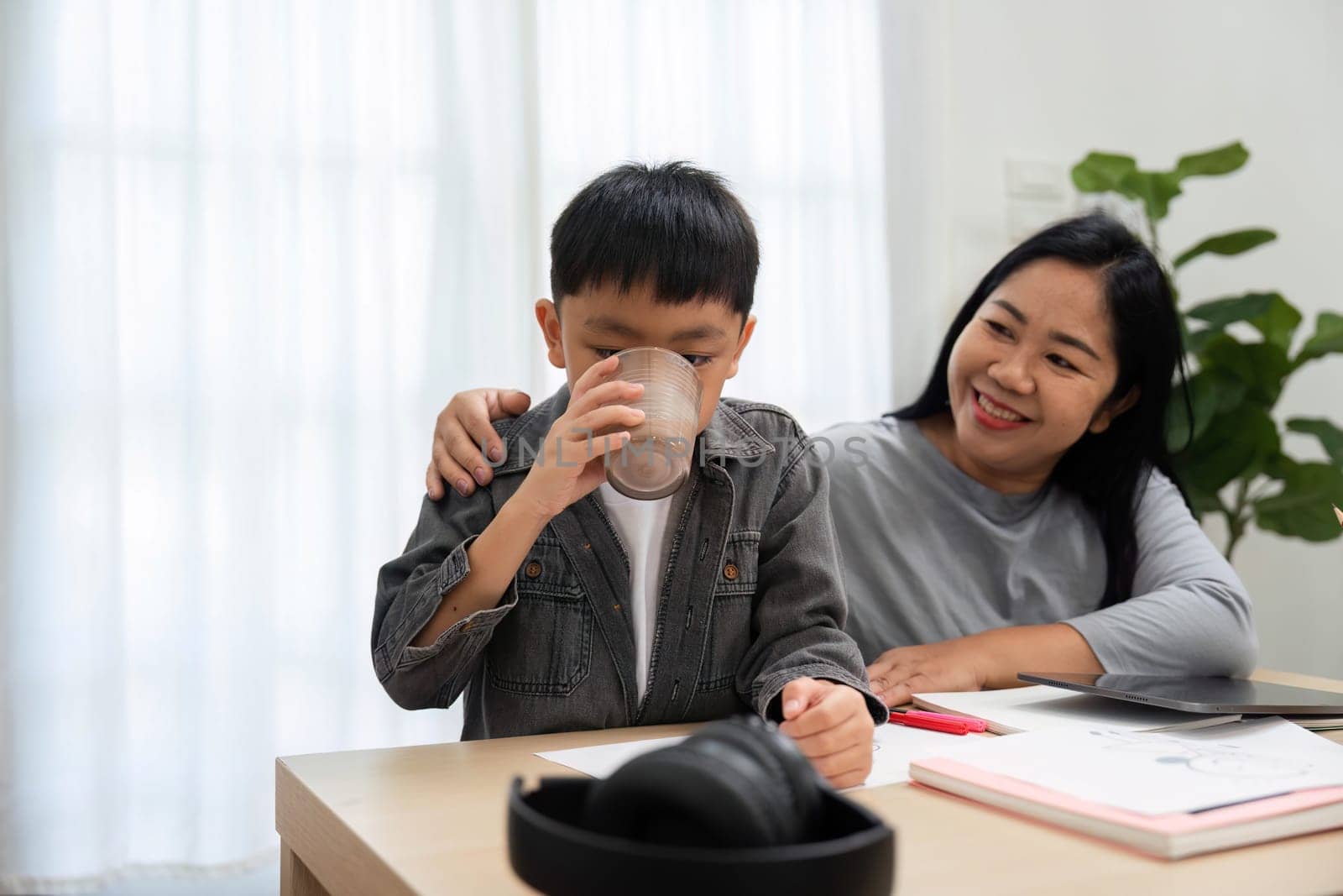 A mother reminds her son to stay hydrated during study time, providing him with a drink and offering a comforting presence to help him focus and relax.