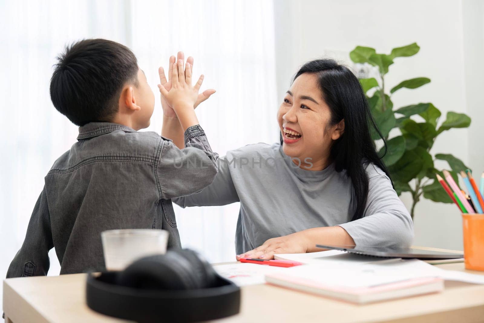 A cheerful mother and her son celebrate their back-to-school preparations with a high-five, showcasing their close relationship and excitement for the upcoming school year.