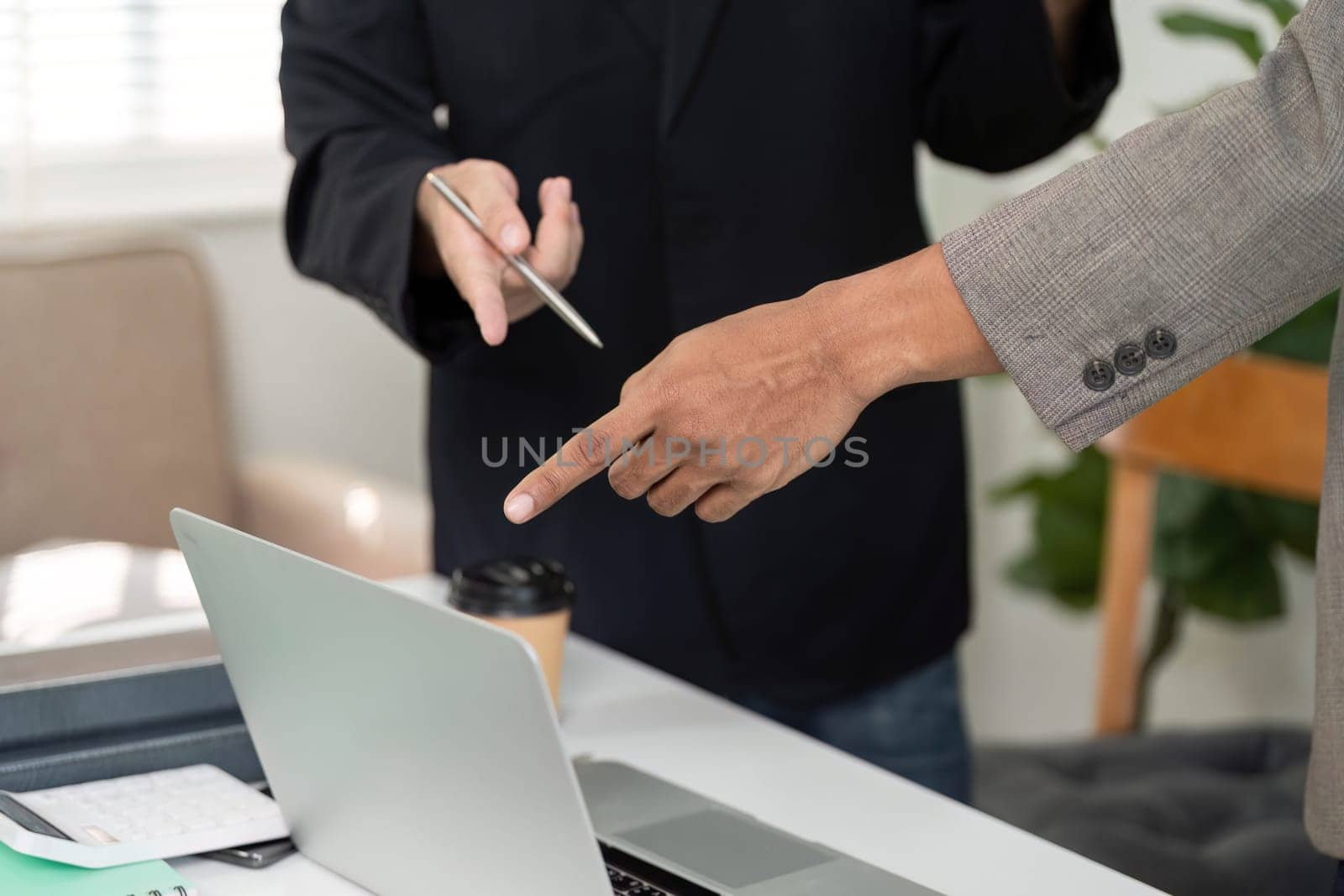 In a collaborative setting, two men point at a laptop screen, emphasizing key points while discussing project details and strategies.