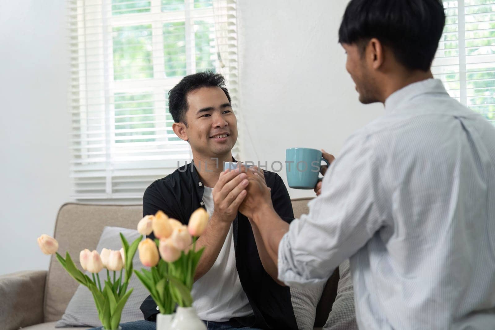 A couple shares a tender moment, exchanging coffee cups and smiles. Their interaction highlights the simple joys of everyday life in an LGBT relationship, emphasizing love and connection.