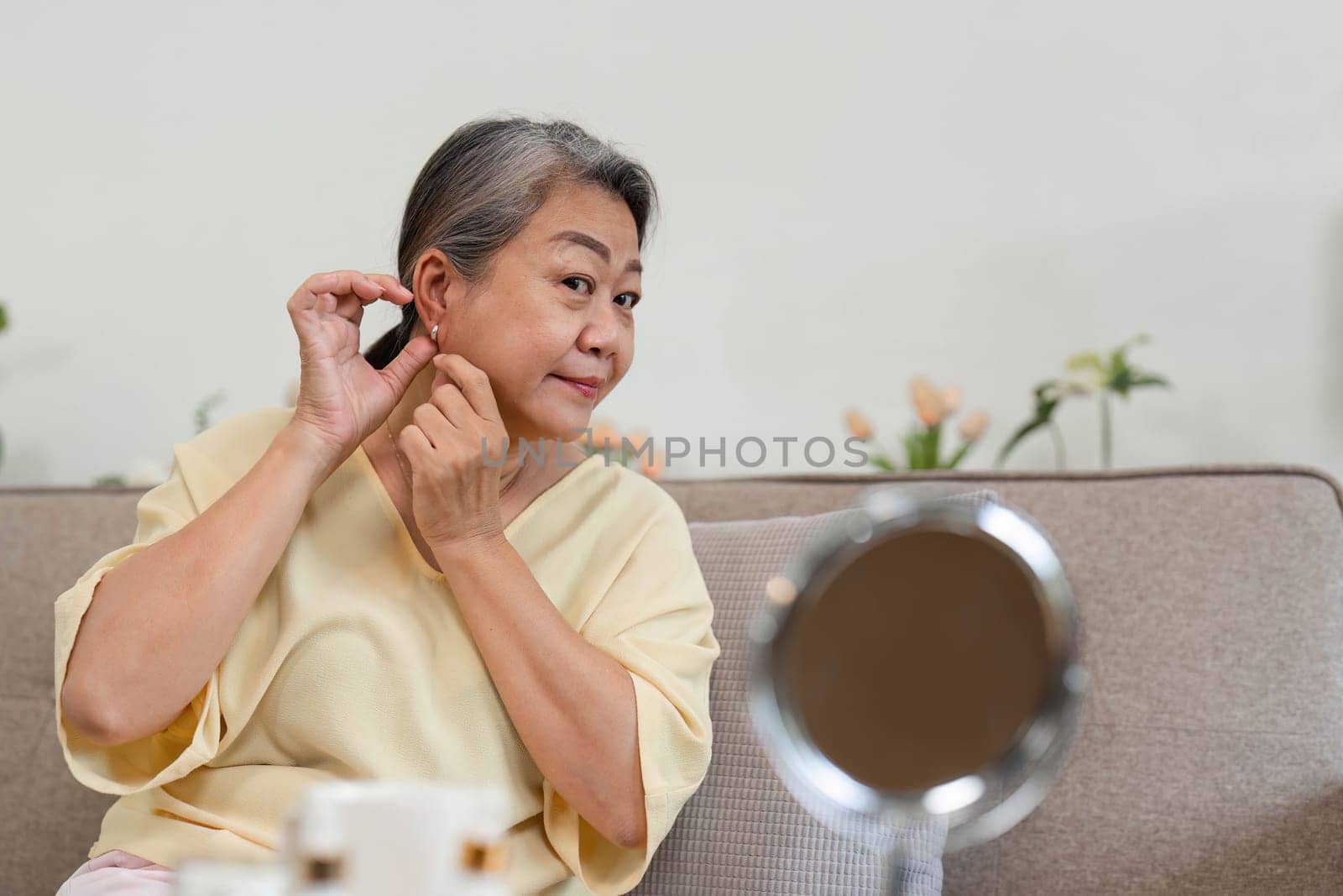 A mature woman enhances her beauty by putting on earrings, enjoying her personal grooming routine in a cozy home environment.