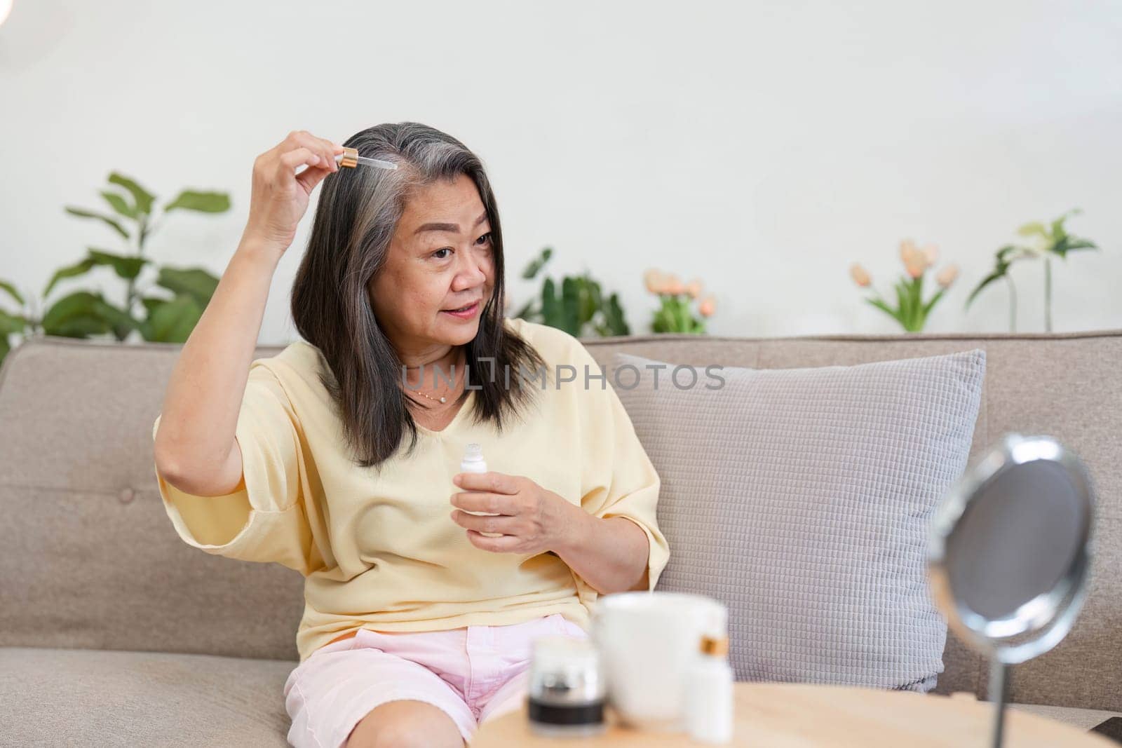 A mature woman applies hair serum, embracing her beauty routine and showcasing age diversity in personal care.