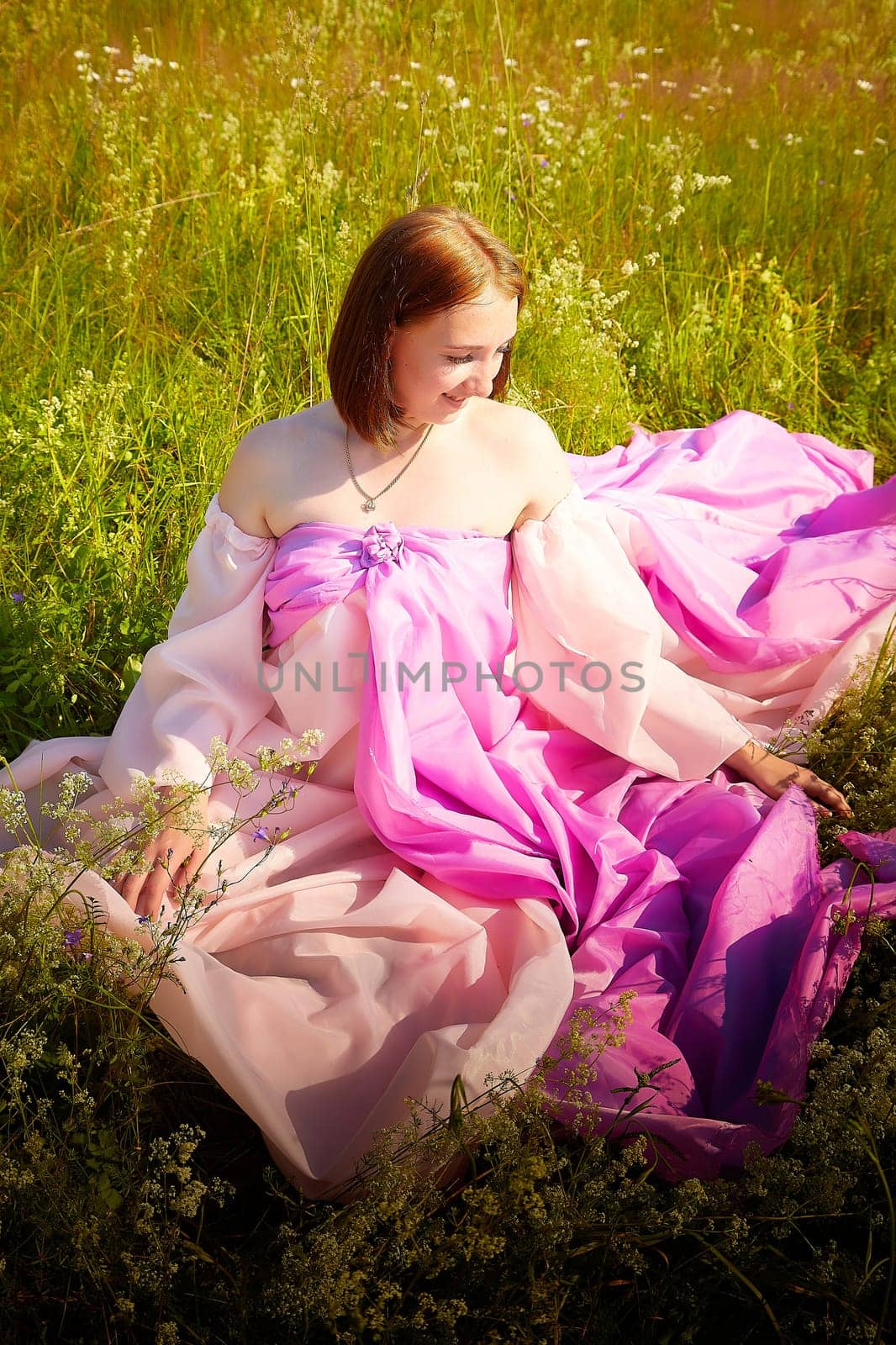 A woman enjoys a moment of tranquility, dressed in a flowing pink gown, amid lush wildflowers under warm sunlight.