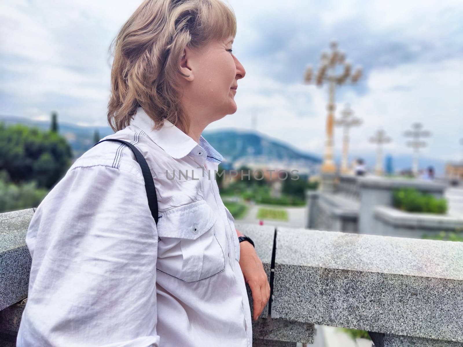 Blonde woman smiling softly while looking out over a picturesque view during her travel adventure, enjoying the outdoor experience.