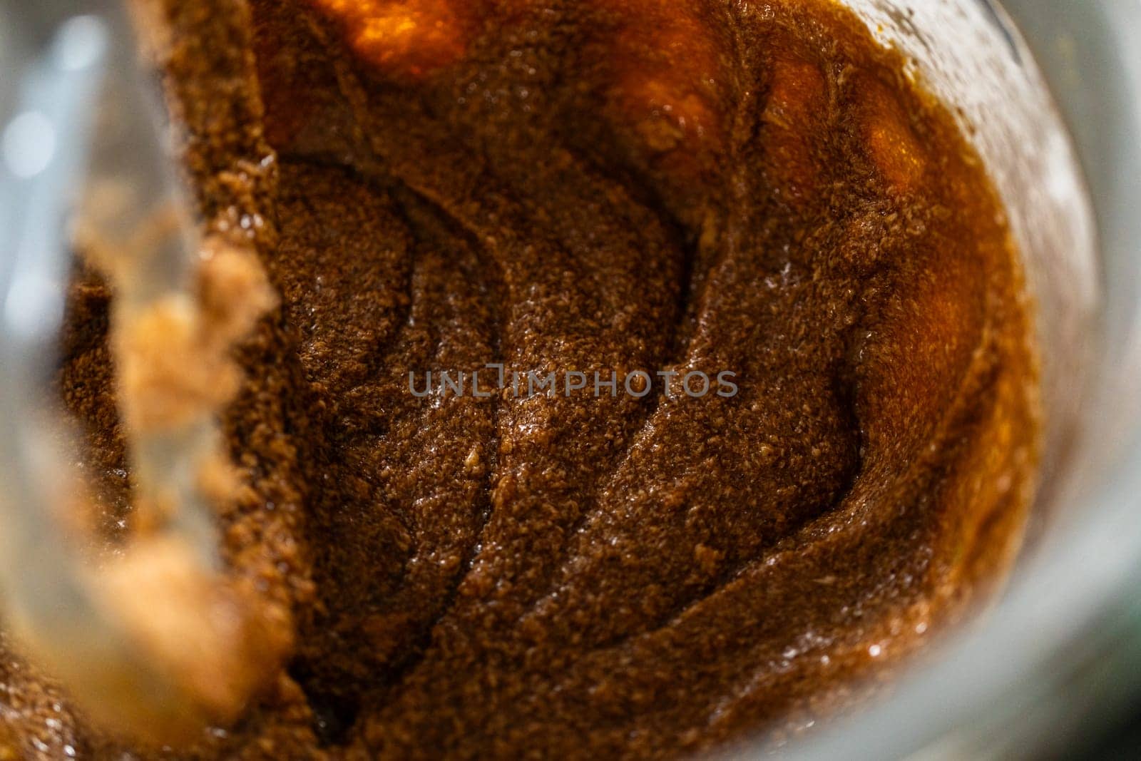 The mixer bowl shows a rich, dark molasses added to the creamed butter and sugar. The molasses is beginning to integrate, creating a deep brown, aromatic mixture.