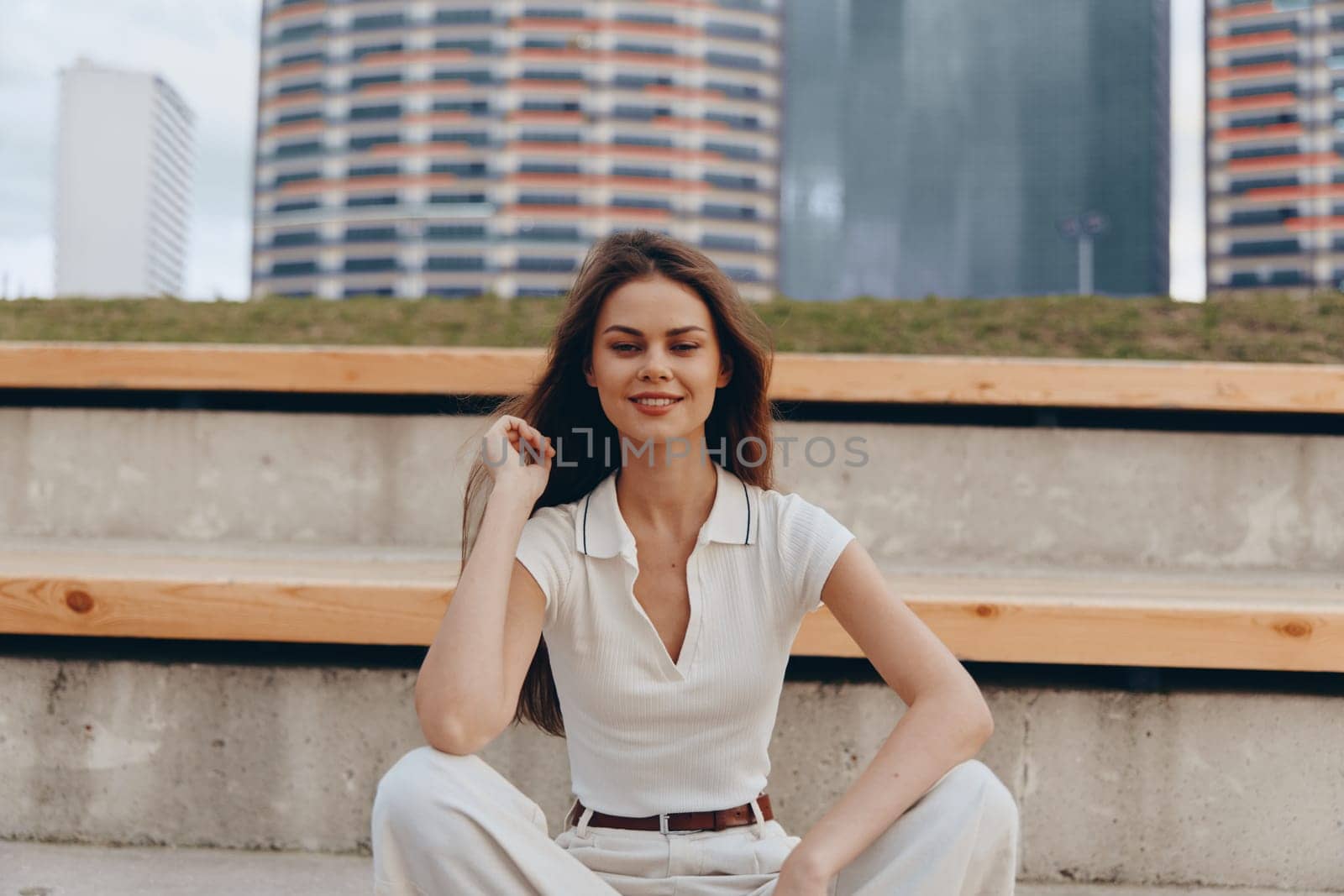 A self-assured woman in business wear smiles while sitting outdoors in a vibrant city environment, showcasing confidence and professionalism. The urban scene enhances her motivated expression and business-focused theme.