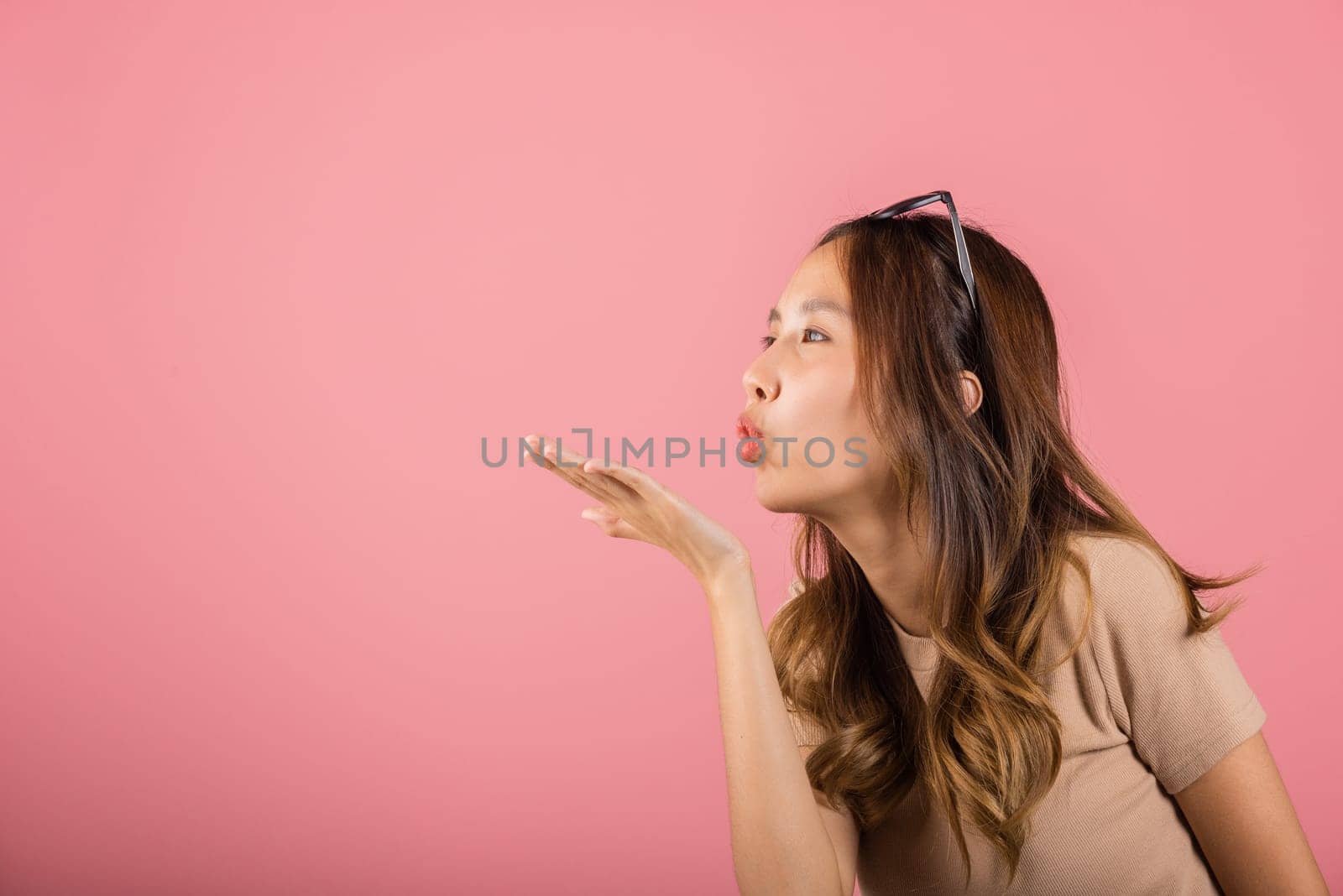 Asian happy portrait beautiful cute young woman teen standing blowing kiss air side something on palm hands expresses her love looking to camera studio shot isolated on pink background with copy space