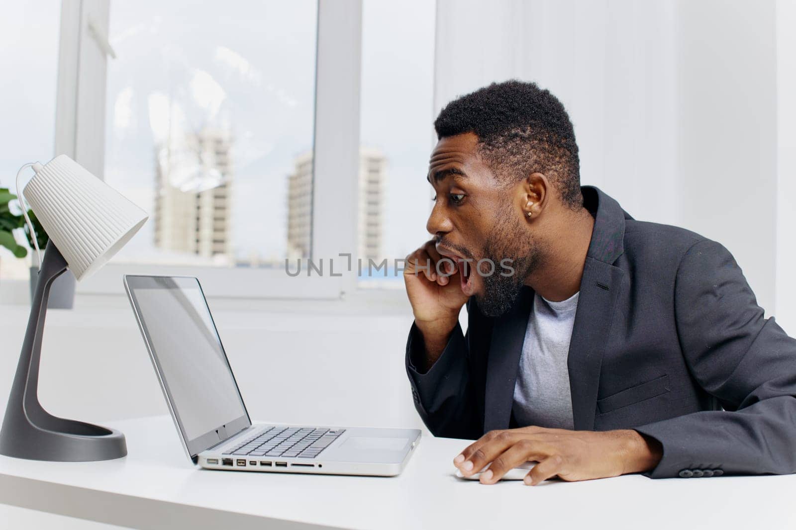 Professional businessman in formal suit diligently working on a laptop at an office desk surrounded by documents and coffee cup.