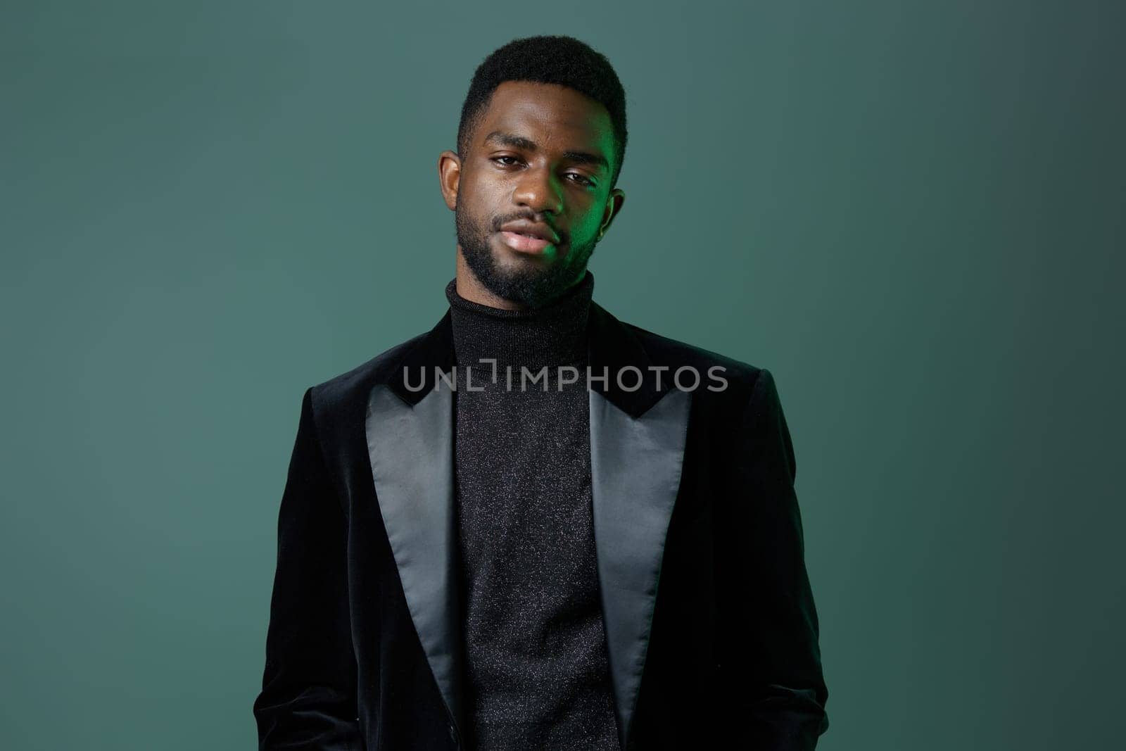 A confident businessman in a sleek black suit and turtleneck stands against a vibrant green background, exuding sophistication.