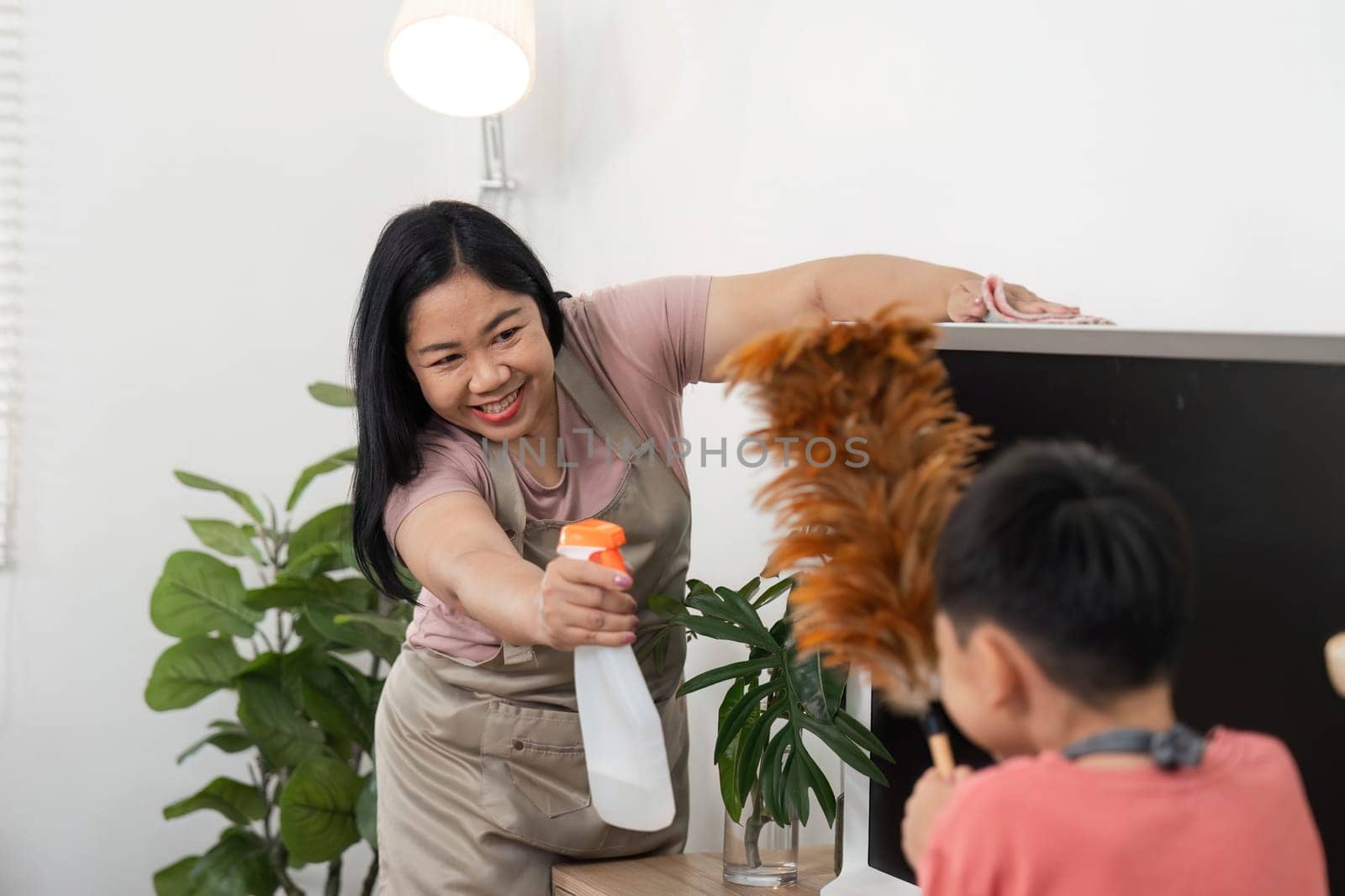 A child joyfully participates in home cleaning, using a feather duster on a TV, highlighting the importance of involving kids in household chores.