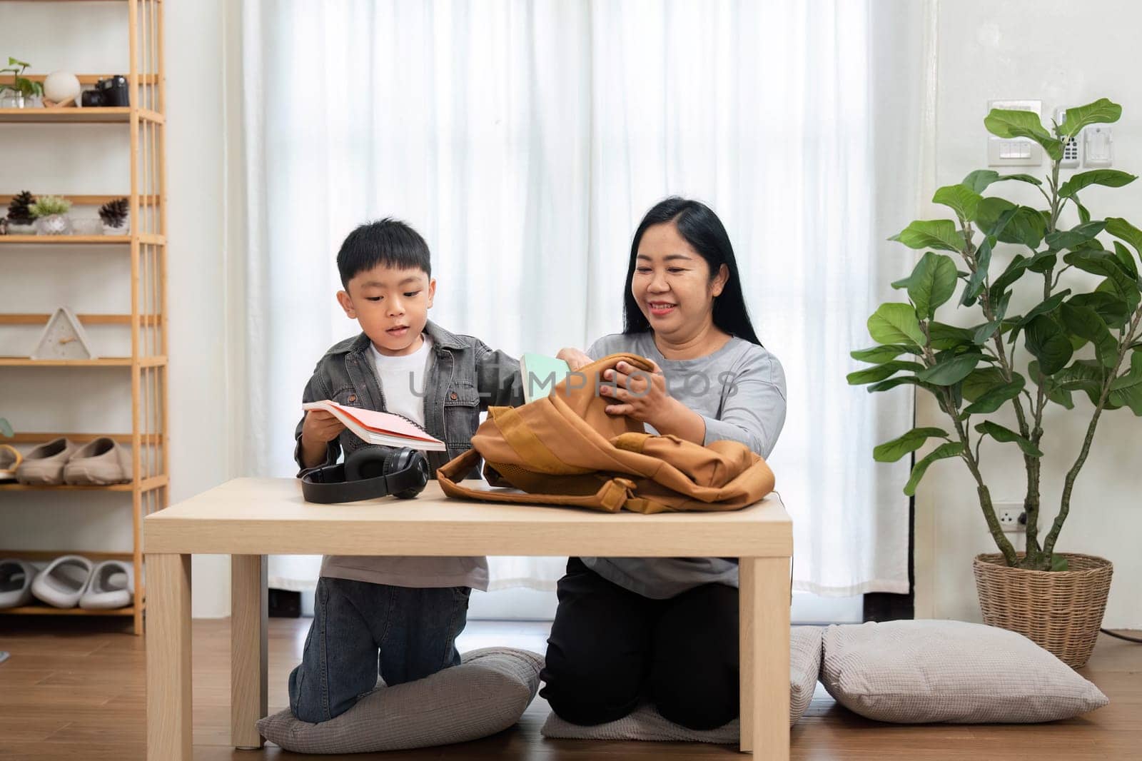 A caring mother and her son are getting ready for the new school year. The mother assists her son with packing his backpack, ensuring he has all the necessary supplies for a successful start.