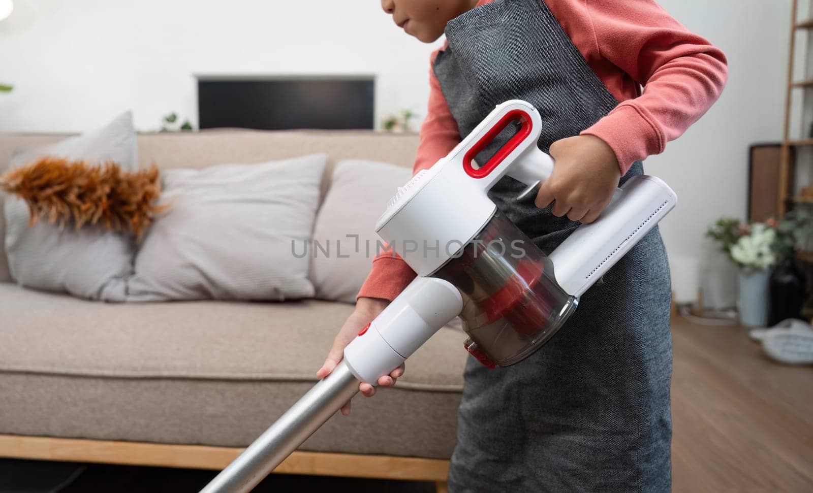 A child actively engages in cleaning the living room with a handheld vacuum, demonstrating responsibility and learning valuable life skills.