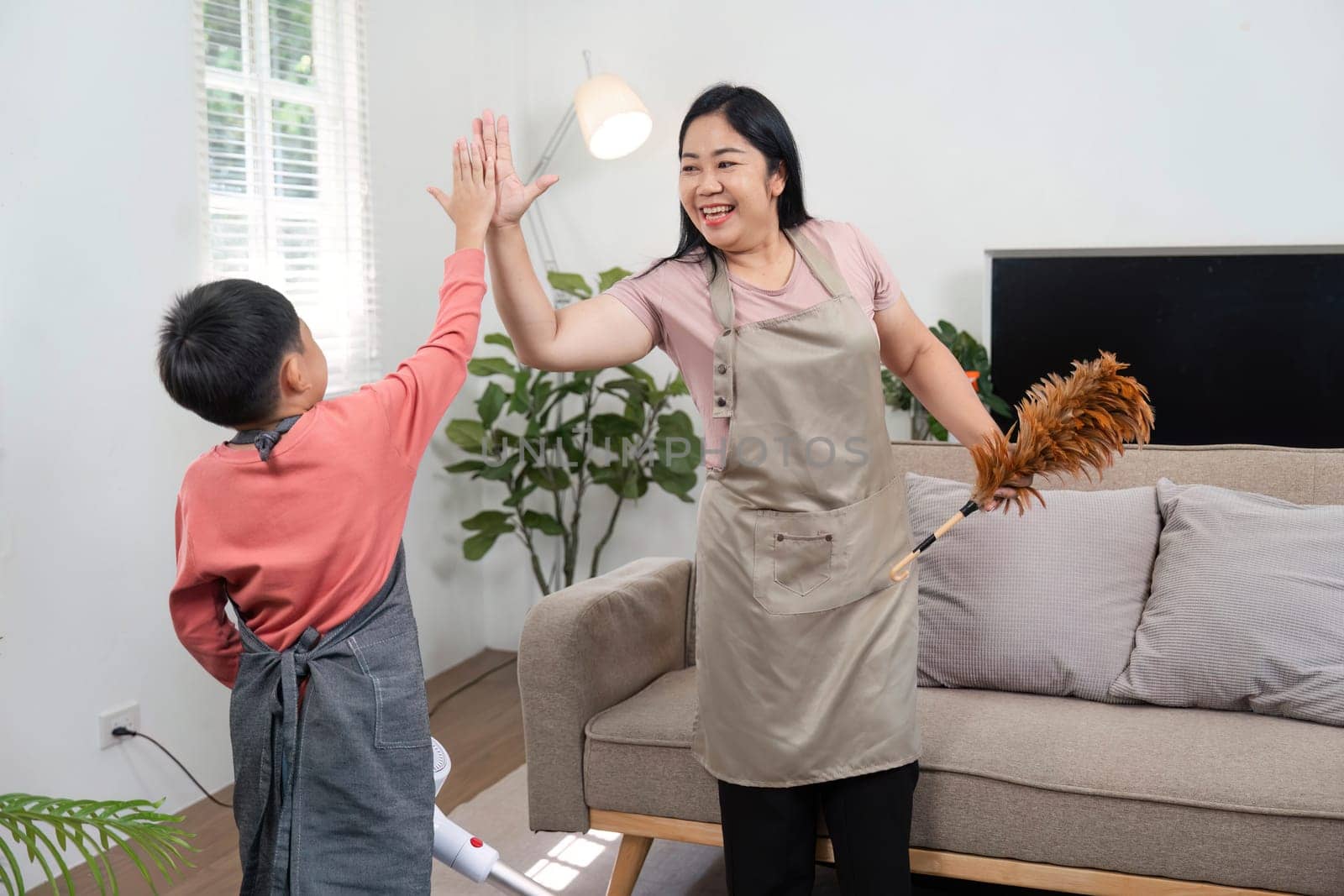 A mother and her son high-five each other while engaging in a fun cleaning session at home, showcasing teamwork and family bonding.